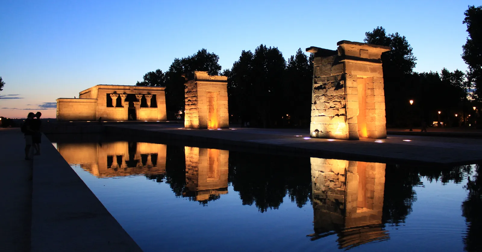 Temple of Debod in Madrid lit at dusk with its reflecting pool in the foreground