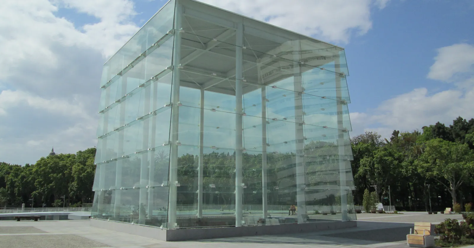 The glass-paneled cube structure of Centre Pompidou Málaga on the Muelle Uno waterfront, with palm trees and a paved plaza around it