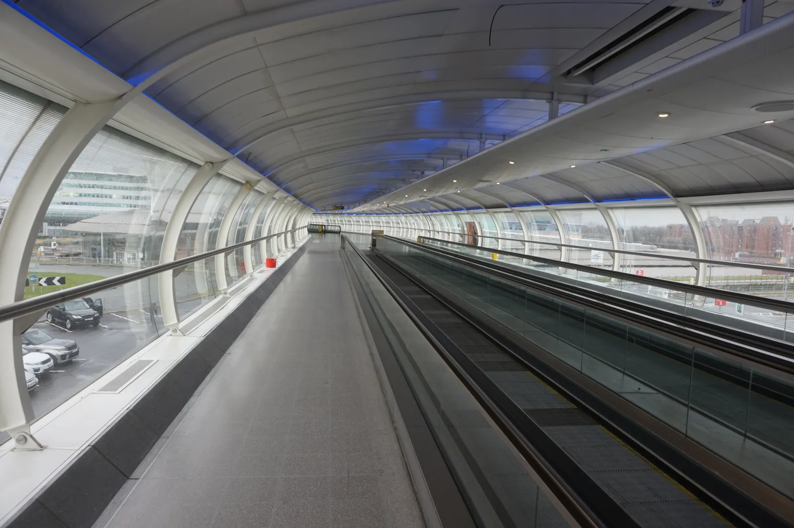 The enclosed Skylink moving walkway at Manchester Airport, with glass walls looking out over the car parks and terminal buildings