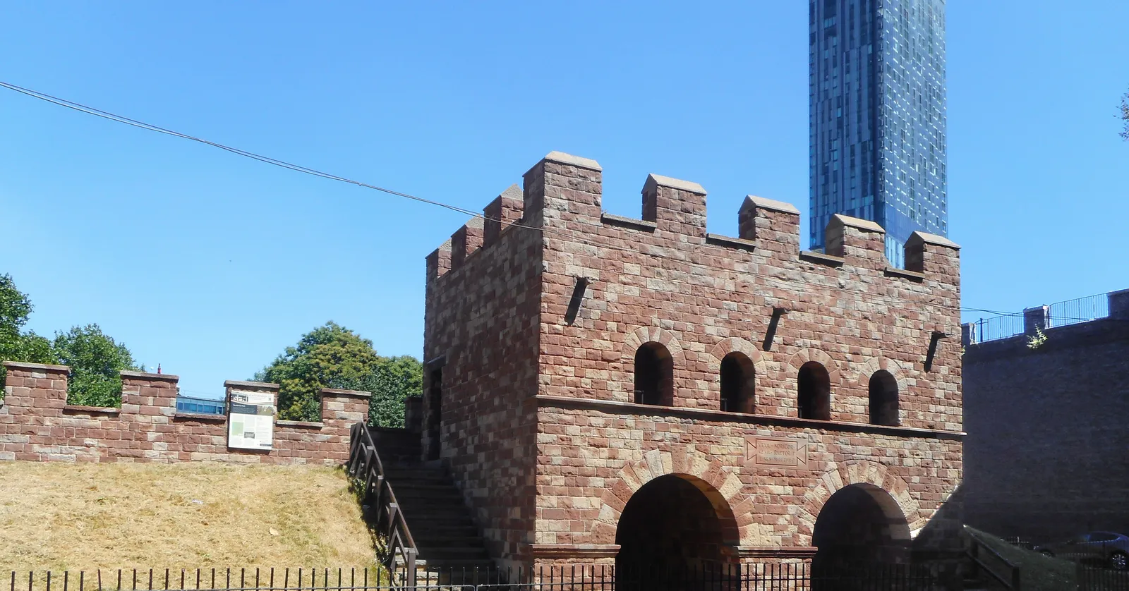 The reconstructed sandstone north gate of the Roman fort Mamucium in Castlefield, Manchester, with a modern glass skyscraper rising behind it