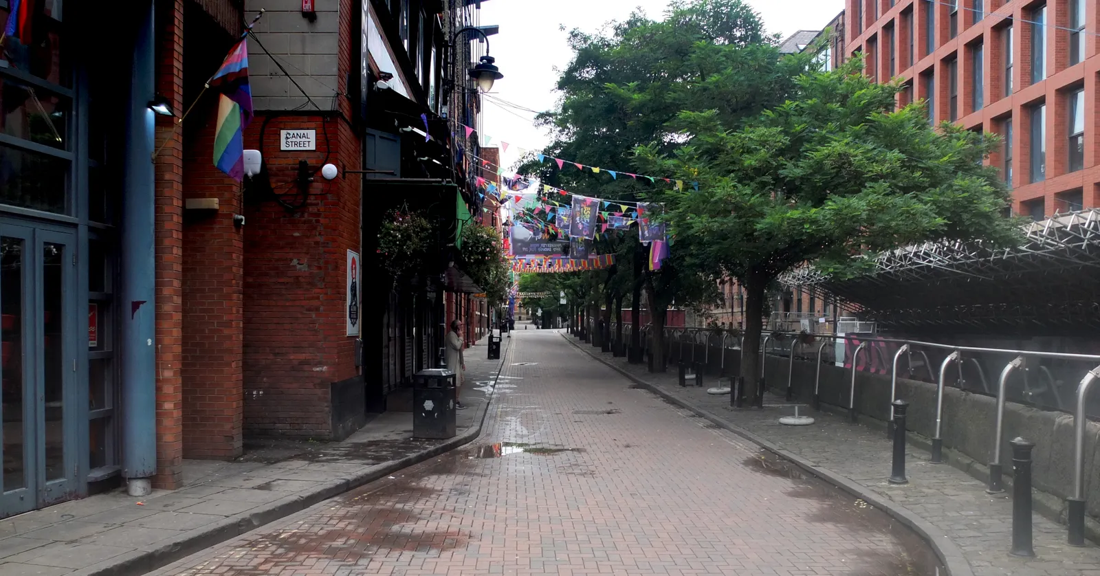 Canal Street's cobbled pedestrian stretch in Manchester, with a rainbow pride flag on a corner building and bunting strung overhead