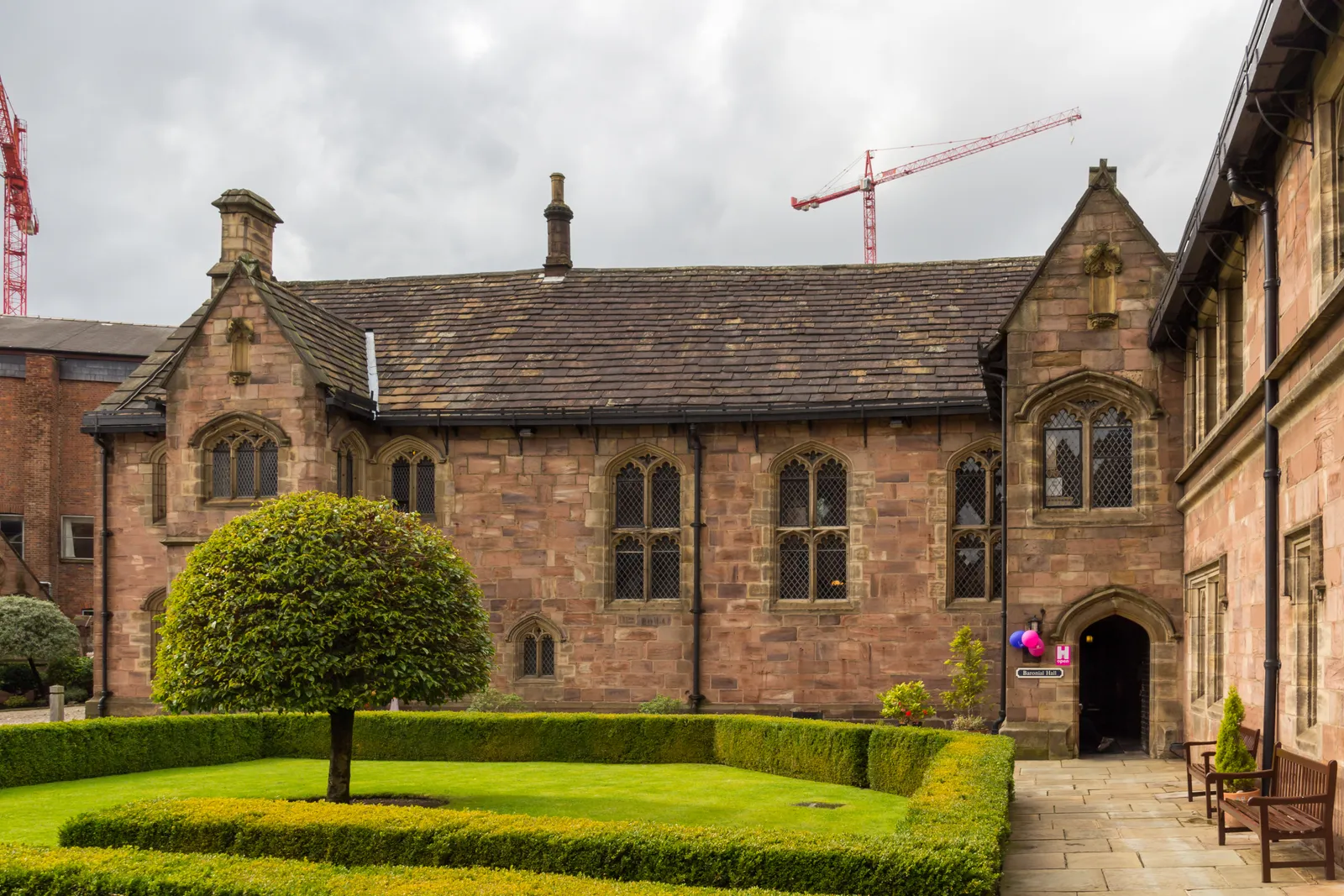 The sandstone medieval buildings of Chetham's College House in Manchester, with a walled courtyard garden and clipped hedges in front