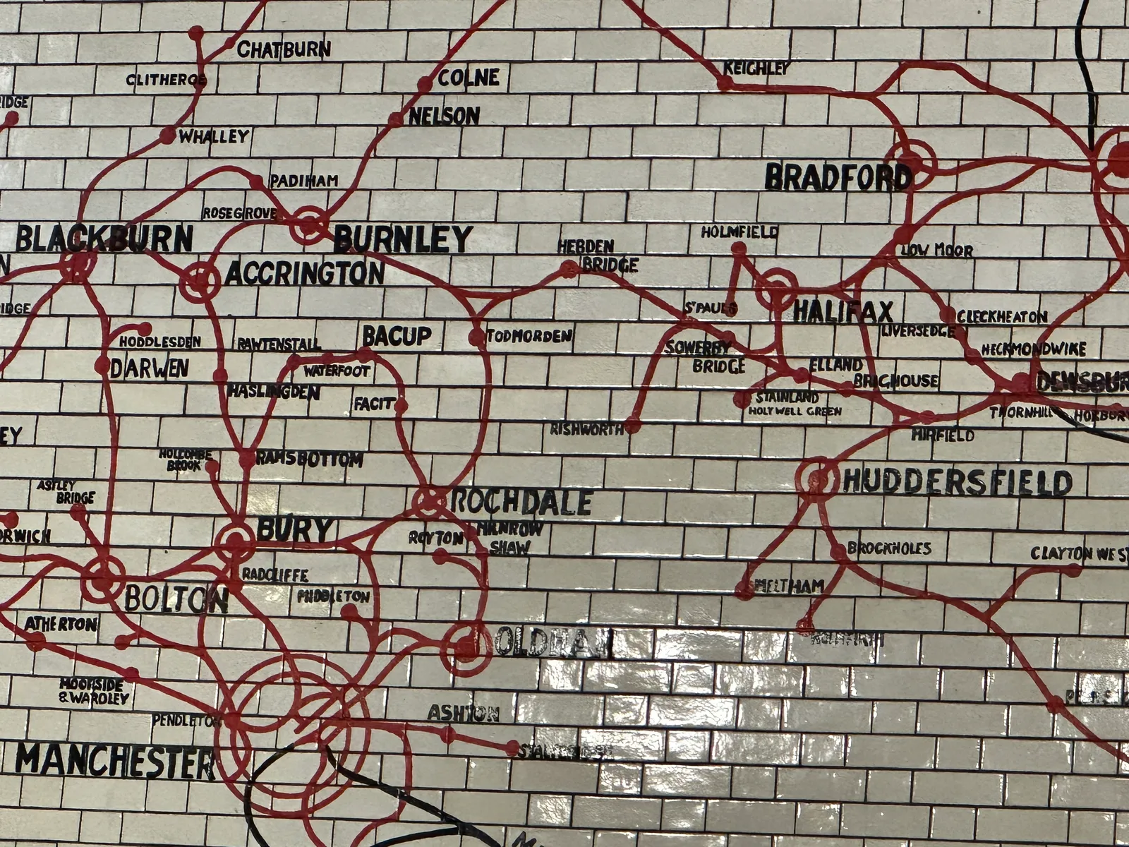 A close-up section of the 1909 tiled mosaic map of the Lancashire and Yorkshire Railway network on a wall at Manchester Victoria station, showing towns including Bolton, Bury and Rochdale