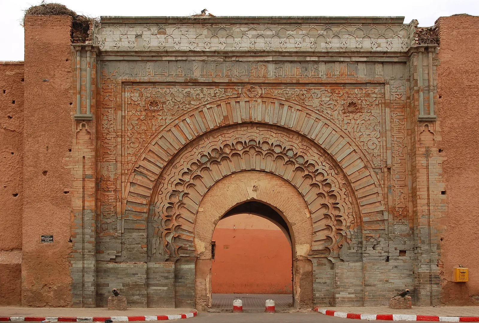 Bab Agnaou in Marrakech, a stone gateway set into a pink earthen wall, its horseshoe arch framed by concentric carved bands and a rectangular panel of carved inscription above