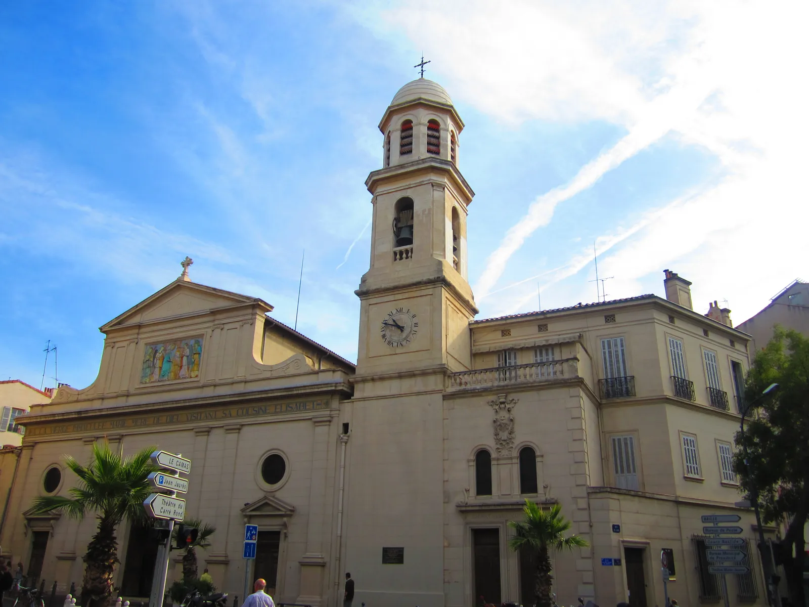 The neoclassical front of Notre-Dame-du-Mont church in Marseille, a coloured ceramic panel set into the pediment above the door and a domed bell tower with a clock beside it