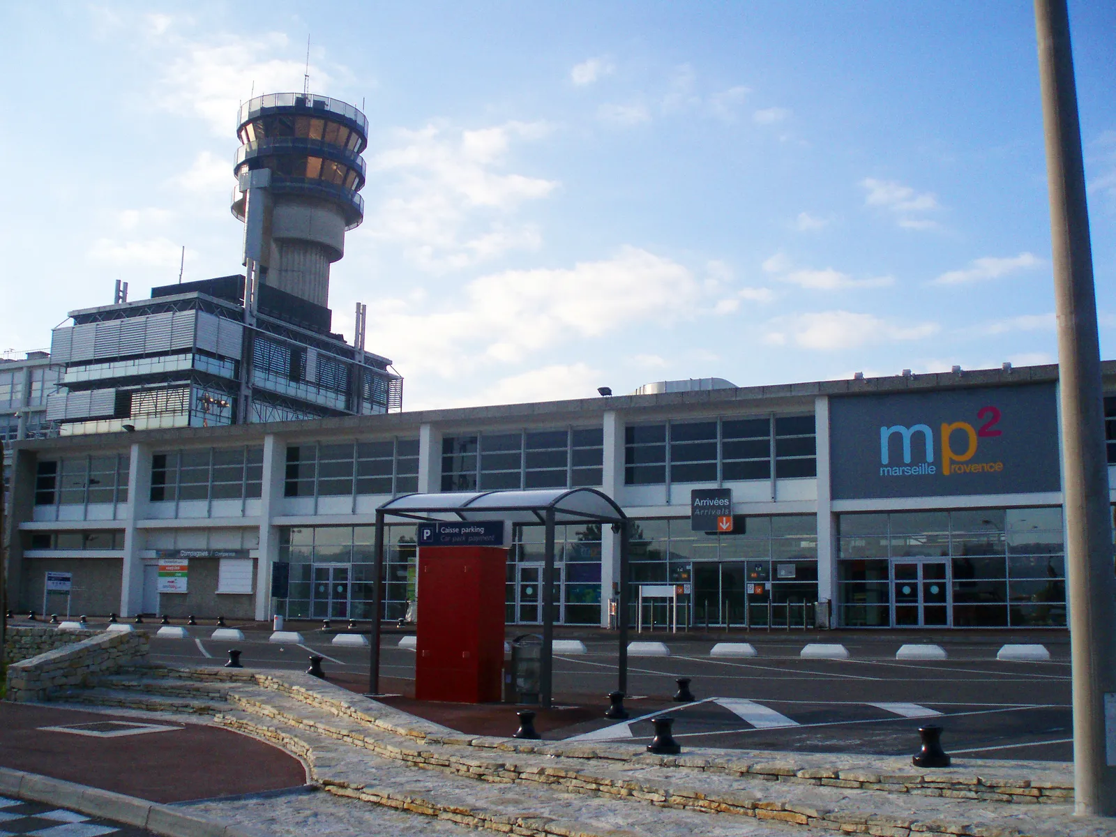 The low glazed frontage of Terminal 2 at Marseille Provence Airport under its mp2 sign, with the airport's ribbed control tower rising behind it