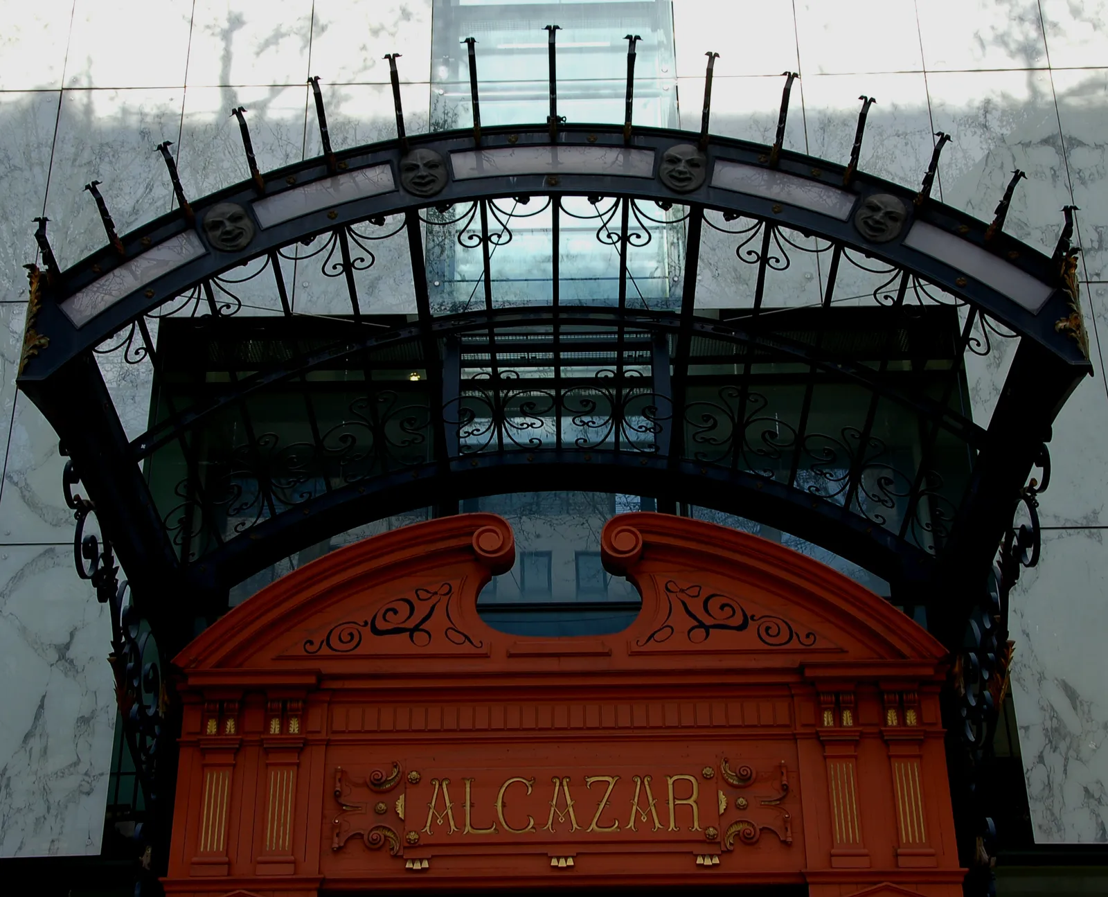 The preserved ironwork canopy over the old Alcazar music-hall entrance in Marseille, its glass roof edged with theatrical masks above a red and gold facade lettered Alcazar