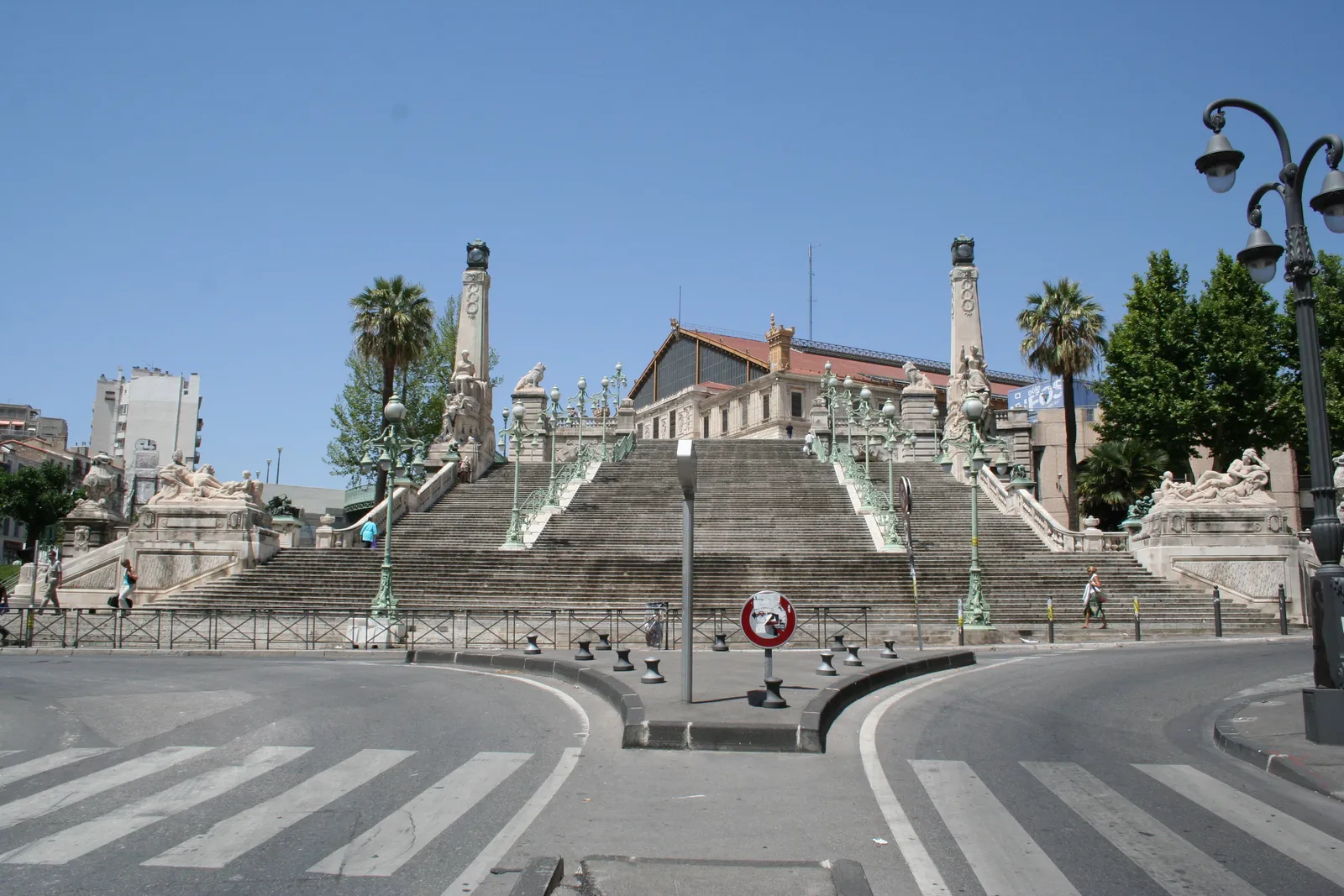 The monumental staircase below Marseille Saint-Charles station seen from the boulevard, its wide stone flights rising between carved pylons and statues to the station building at the top