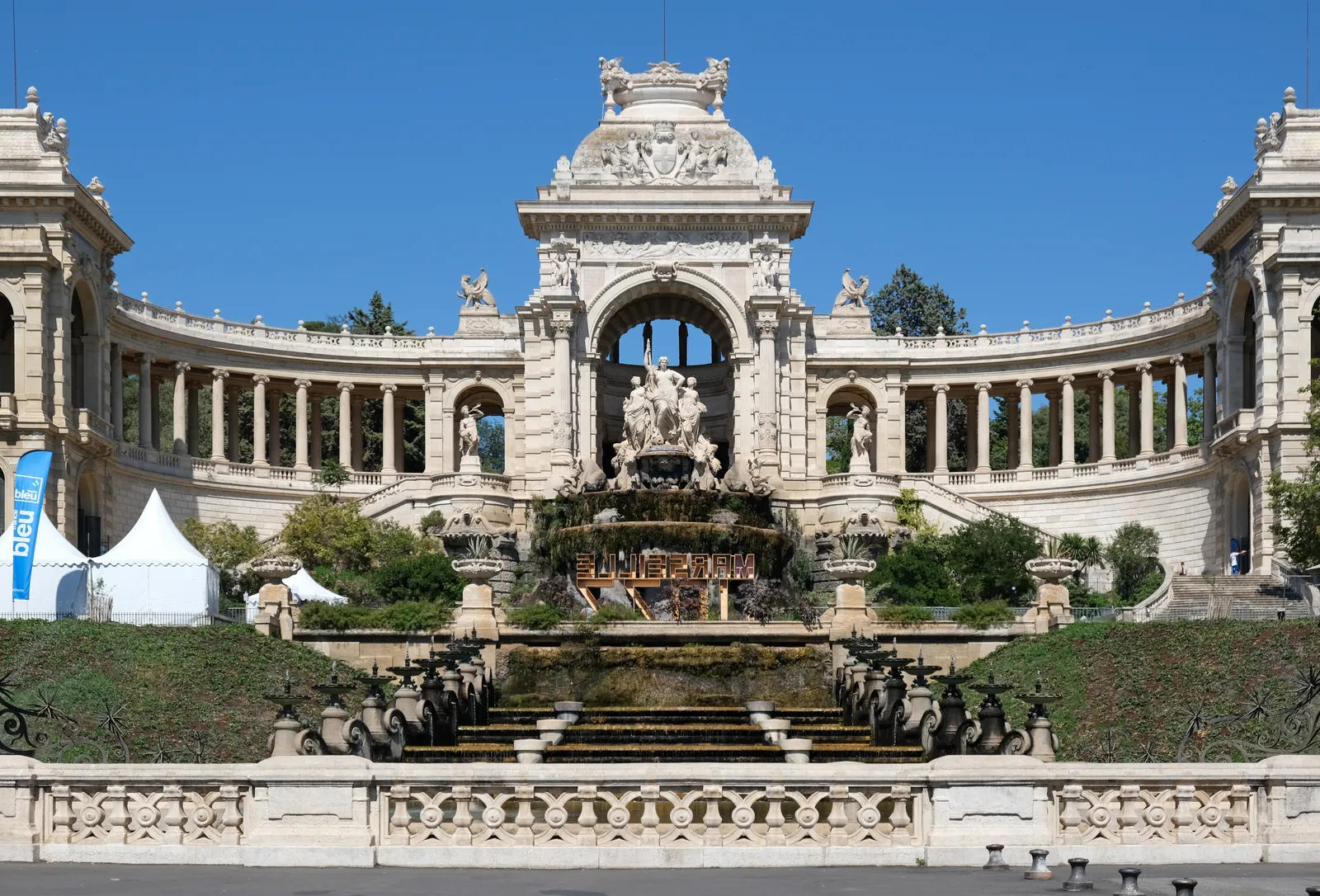 The Palais Longchamp in Marseille, a curved colonnade running out to two wings on either side of a central stone arch, with the tiered water staircase of its fountain below
