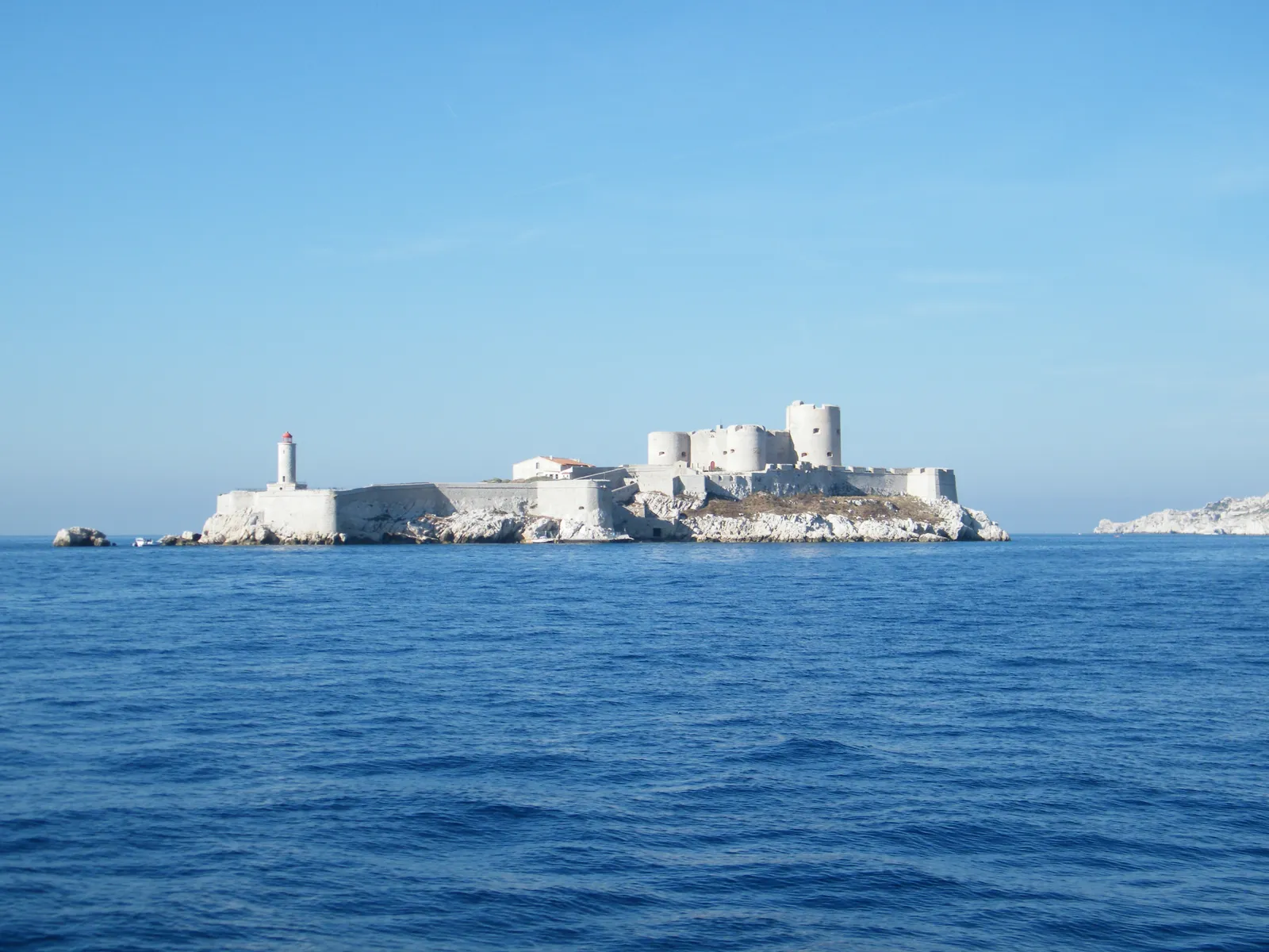 The Château d'If seen from the ferry, a low square fortress with corner towers filling a bare white island under a clear blue sky