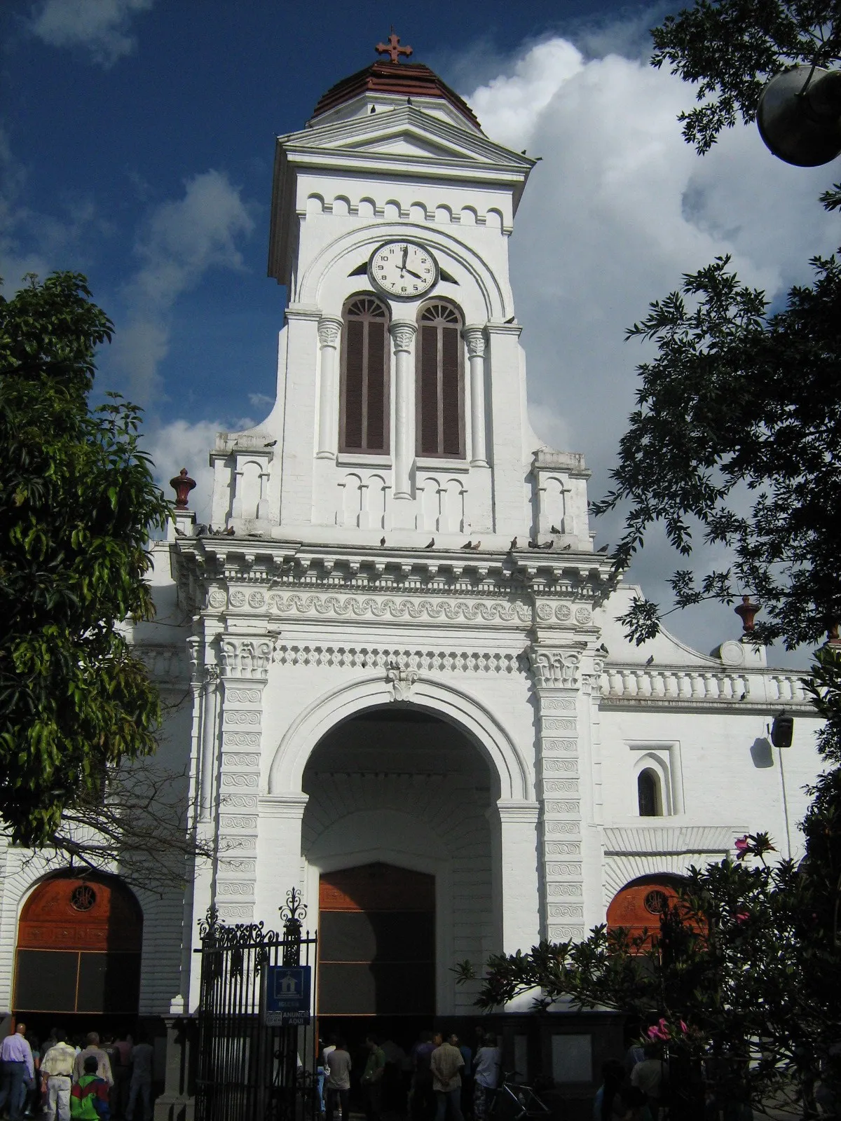 The white bell tower and clock of Iglesia Santa Ana overlooking Parque Principal de Sabaneta under a blue sky
