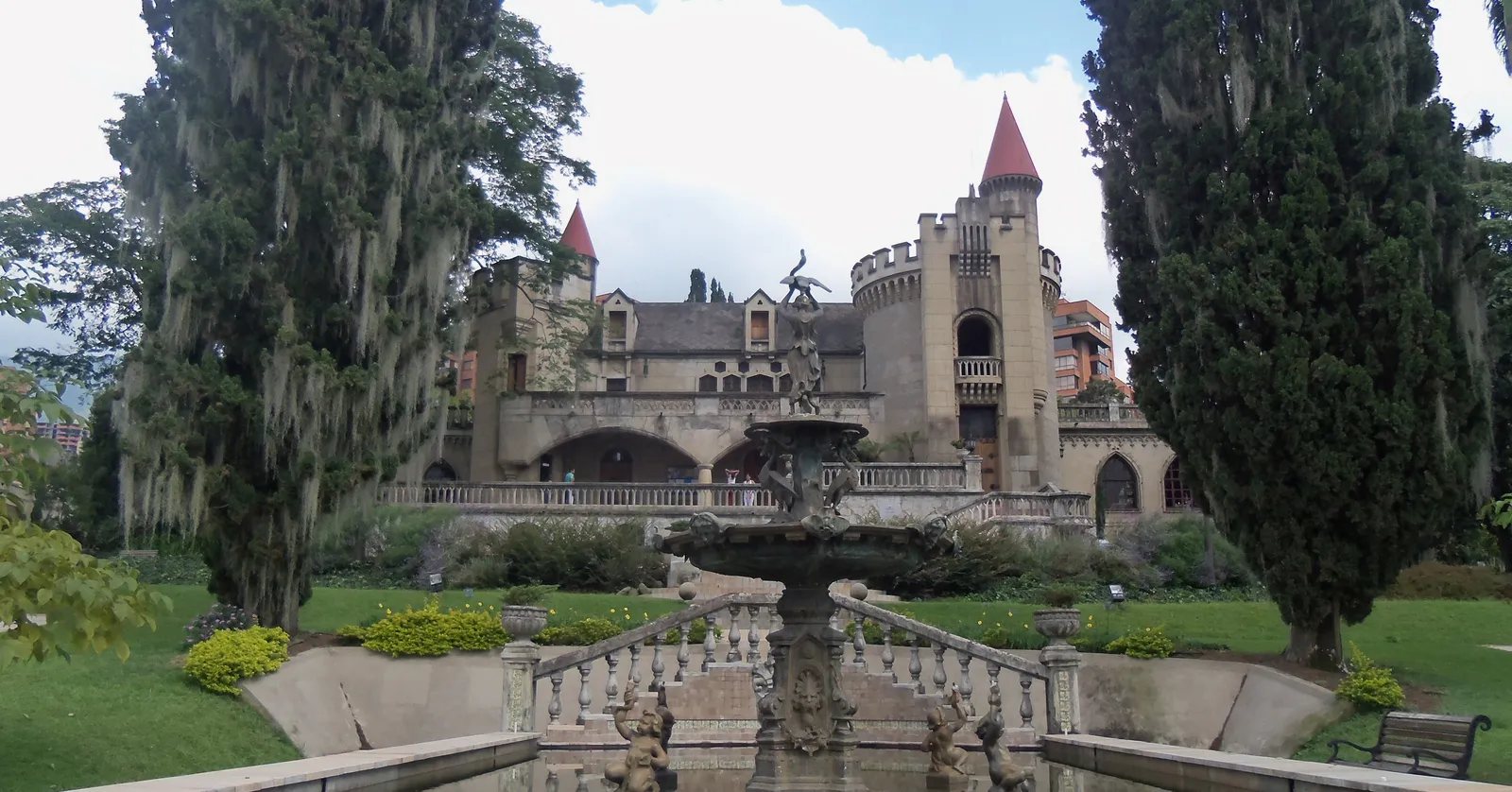 El Castillo's turreted stone facade and terraced gardens in Medellín, with a baroque fountain in the foreground and cypress trees framing the building