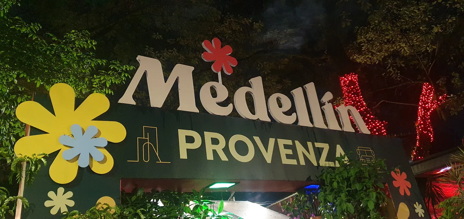 An illuminated Provenza sign over a flower-decorated entrance to Medellín's Provenza nightlife district at night