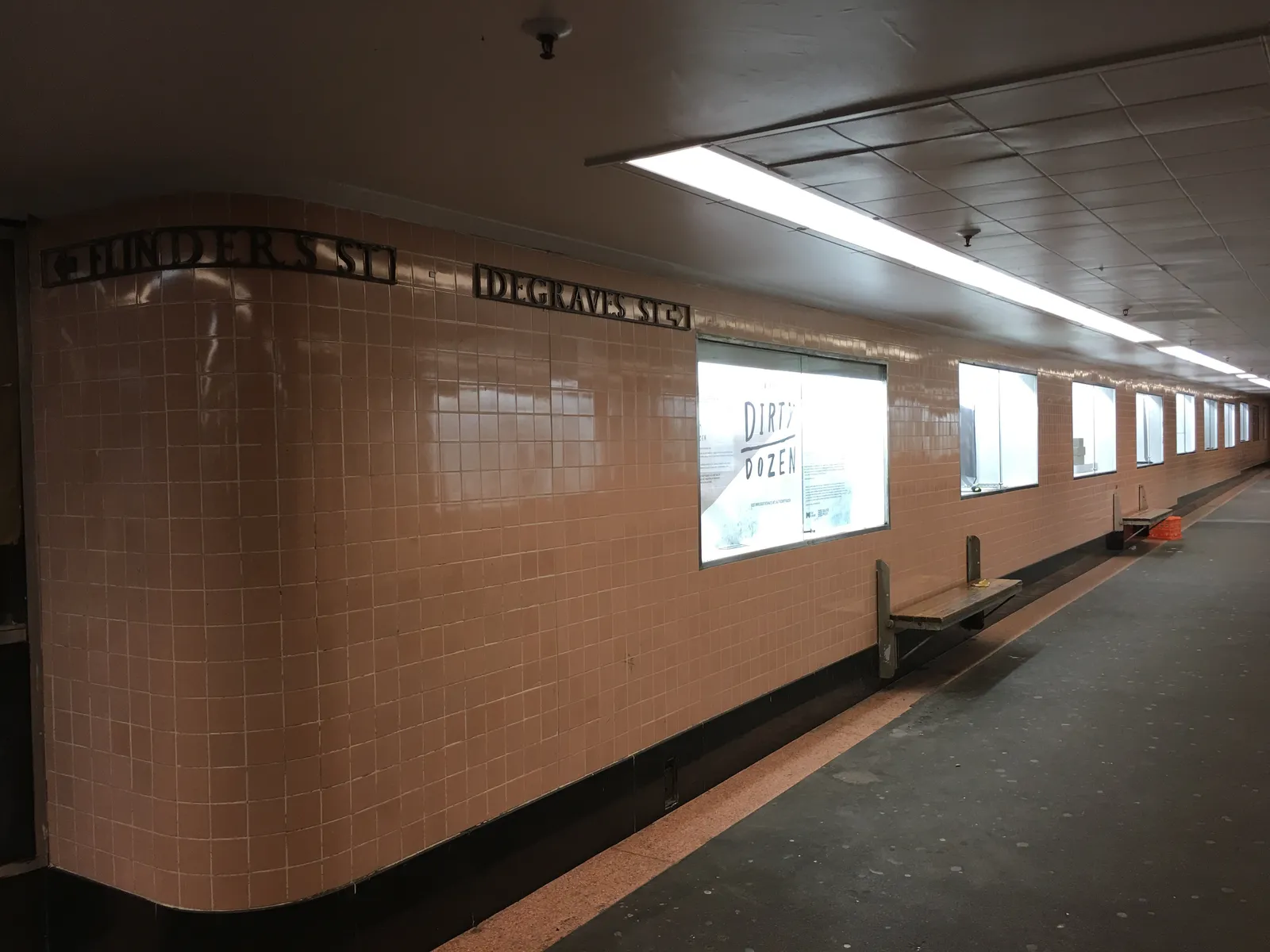 The salmon-pink tiled wall of Campbell Arcade under Flinders Street in Melbourne, with the words Flinders St and Degraves St set into the tiling above lit display cases