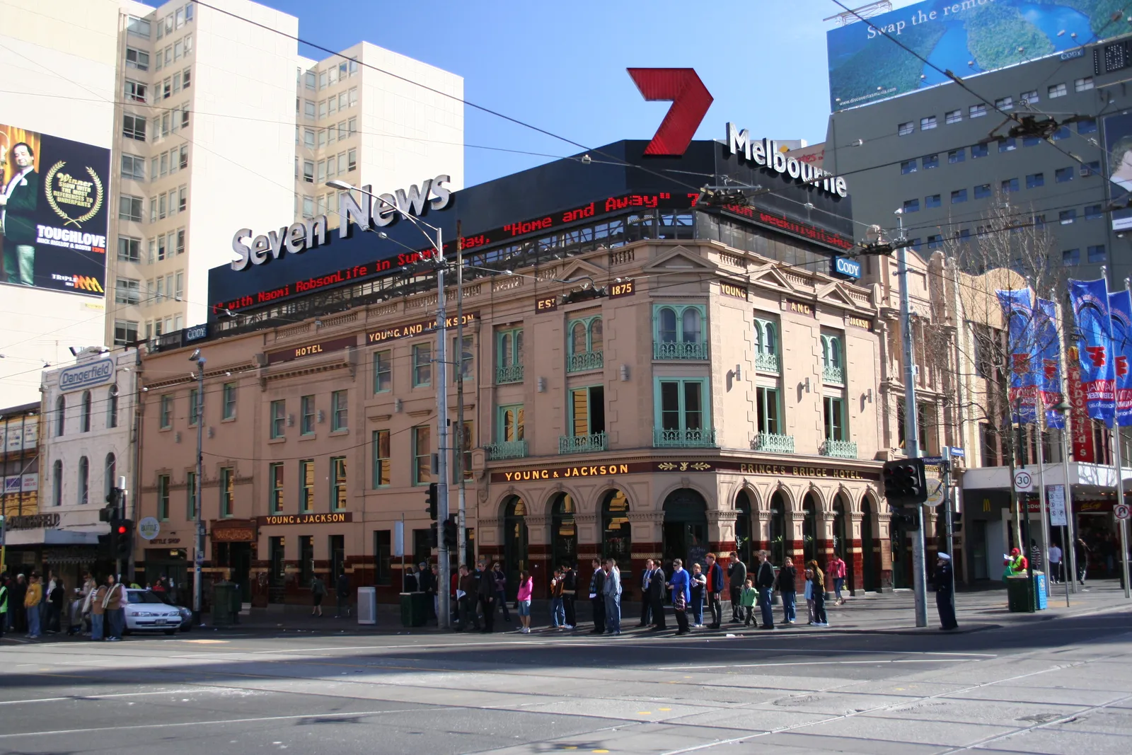 The Young and Jackson hotel on the corner of Flinders and Swanston streets in Melbourne, a two-storey nineteenth-century pub in pink render with green cast-iron balconies and pedestrians crossing in front