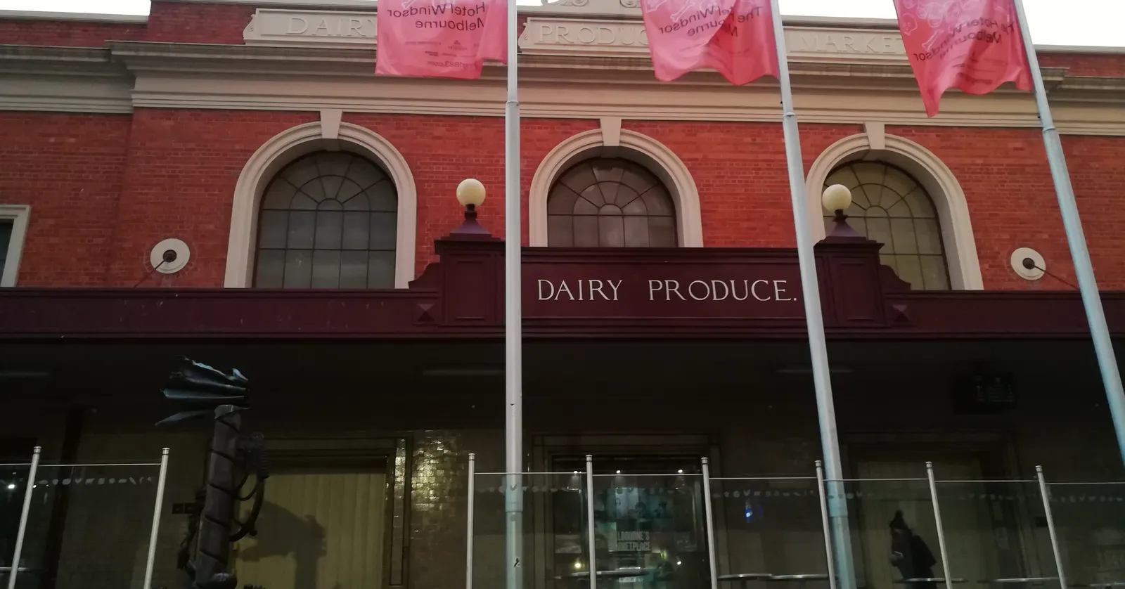 The red brick frontage of the Dairy Produce Hall at Queen Victoria Market in Melbourne, arched windows above a dark awning with the words Dairy Produce set into the parapet