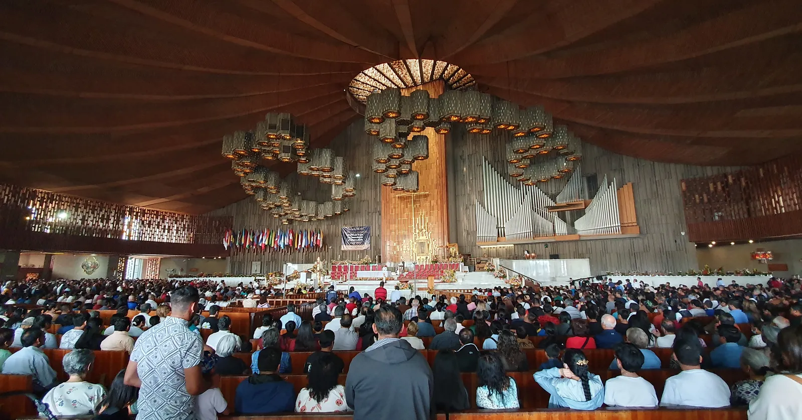 The circular timber-lined interior of the new Basilica of Our Lady of Guadalupe in Mexico City, packed with seated worshippers facing the altar and the framed image above it