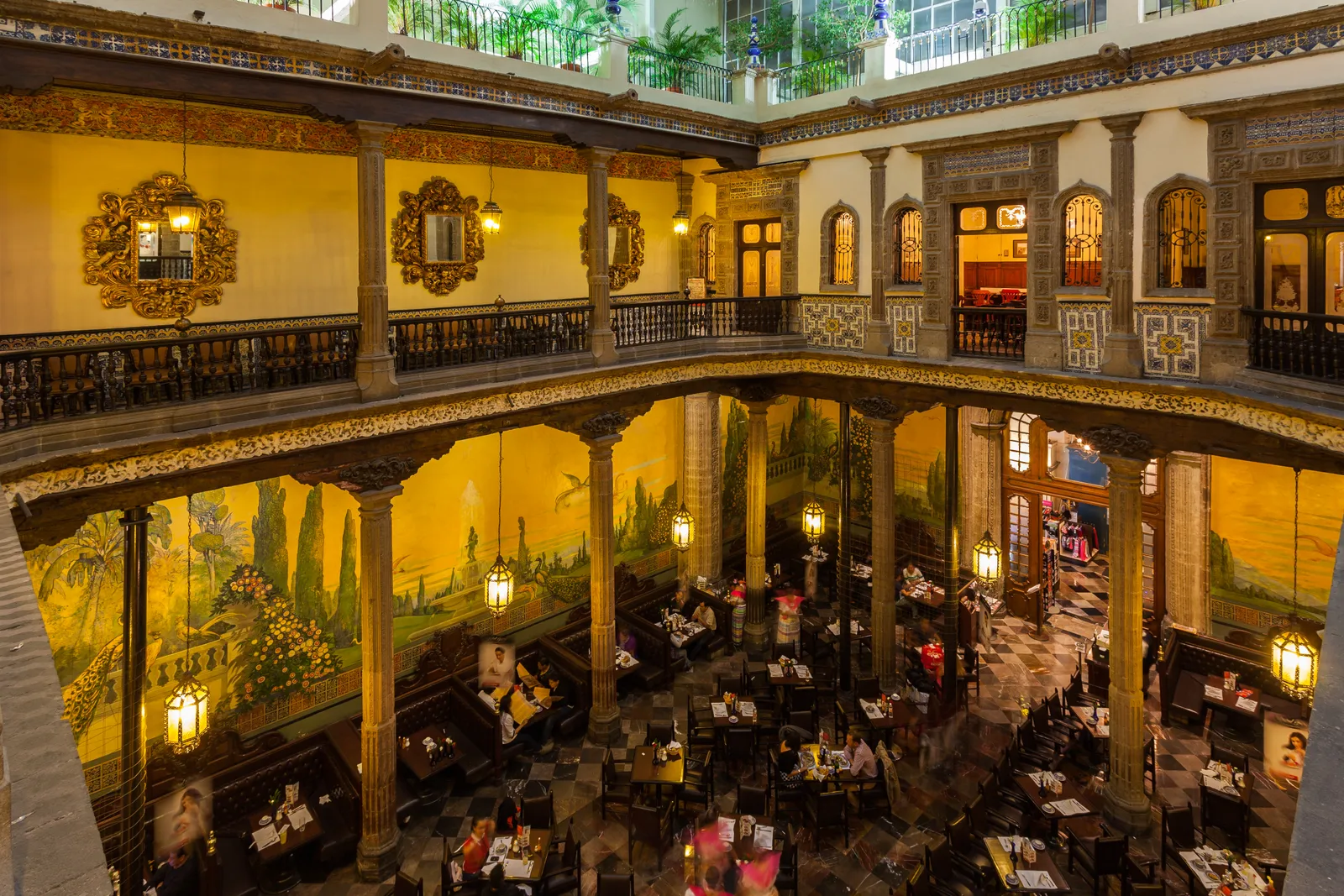 The glass-roofed inner courtyard of the Casa de los Azulejos in Mexico City, now a restaurant, with tiled walls, gilded mirrors and a first-floor gallery of carved wooden balustrades