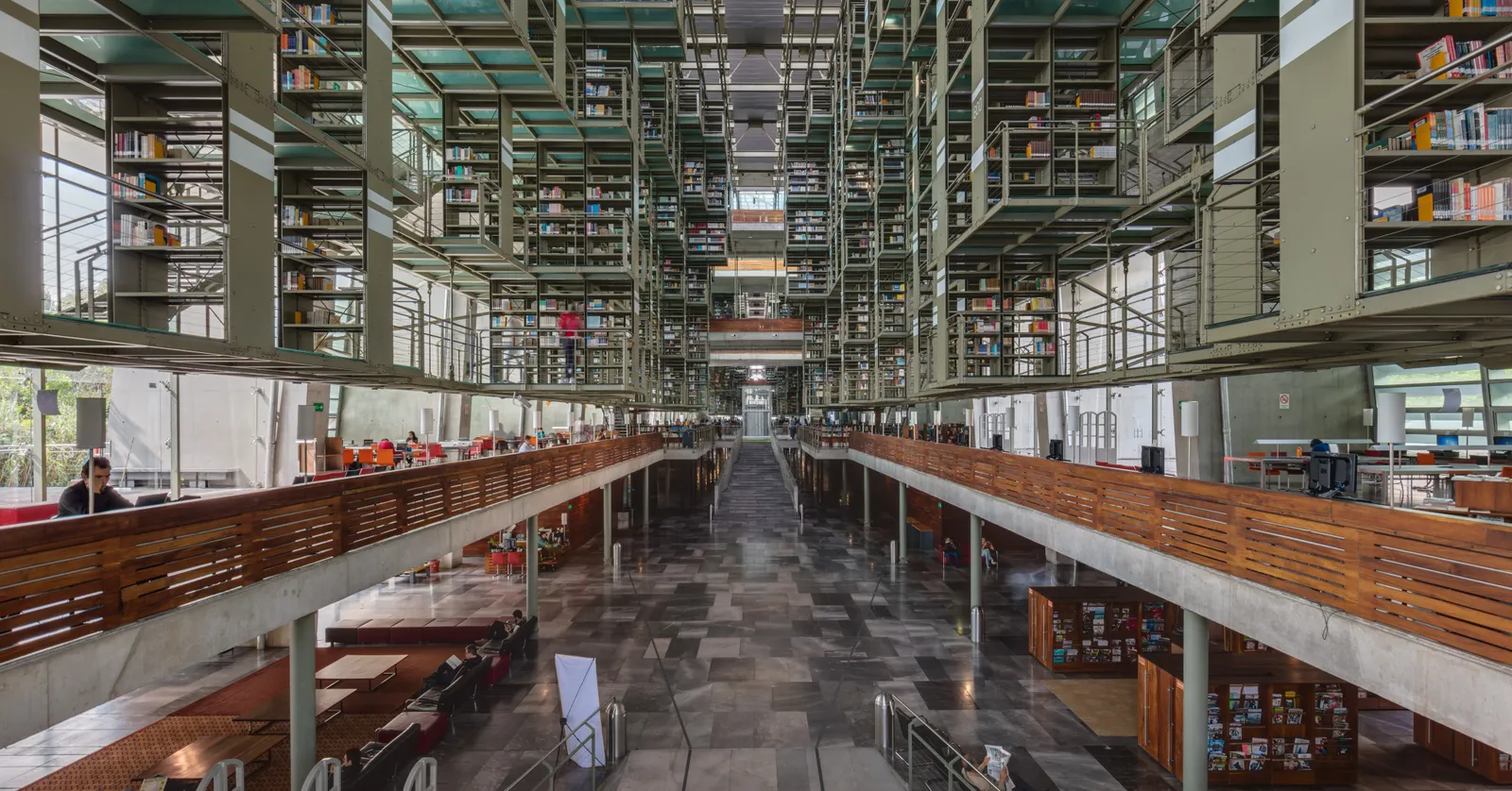 The main hall of the Biblioteca Vasconcelos in Mexico City, with steel book stacks hung in tiers off both side walls above a long central floor lit from a glass roof