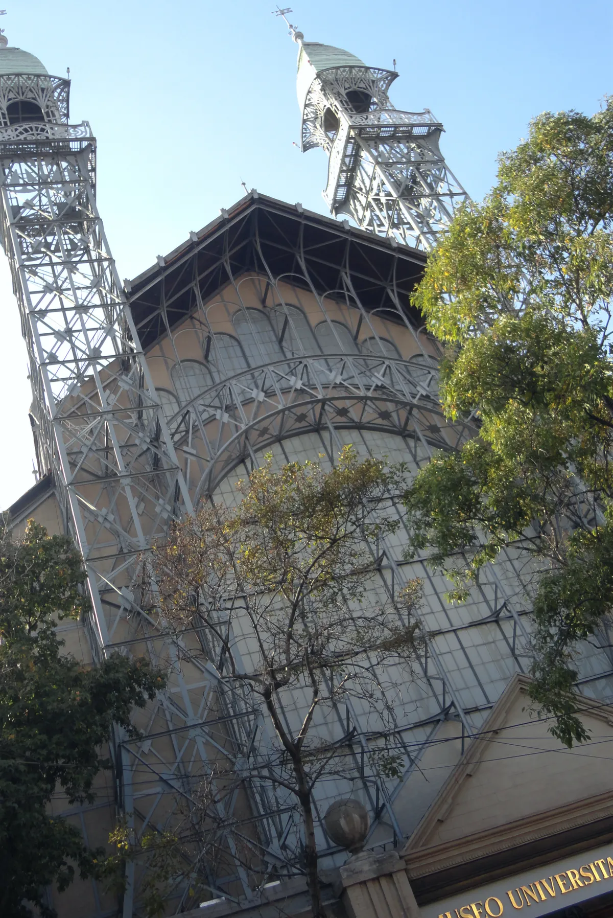 The front of the Museo Universitario del Chopo in Mexico City, a glazed iron hall flanked by two open lattice towers, seen from the pavement below