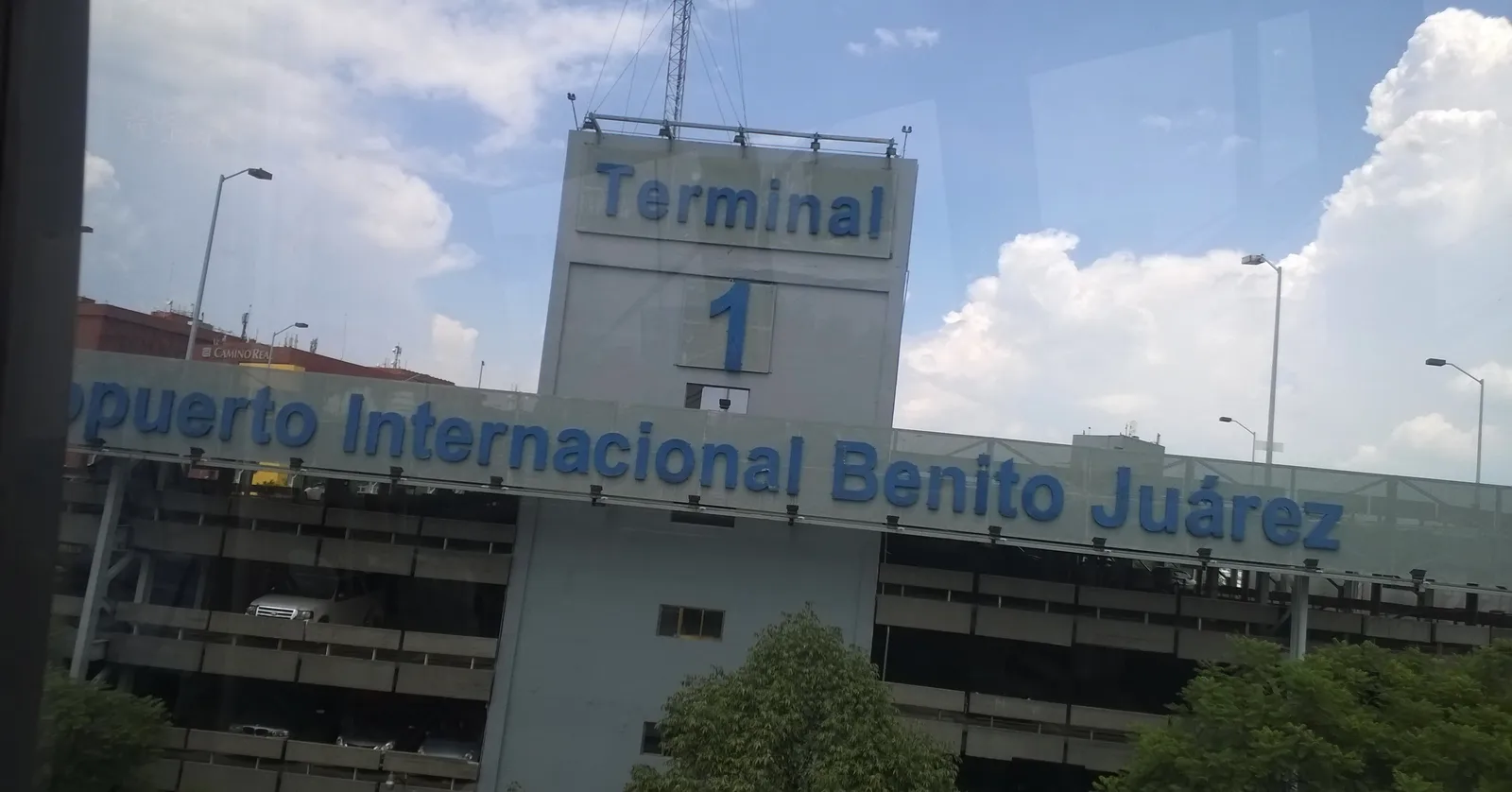 The blue lettering reading Terminal 1 and Aeropuerto Internacional Benito Juárez across the front of the multi-storey car park at Mexico City's airport, under a bright sky