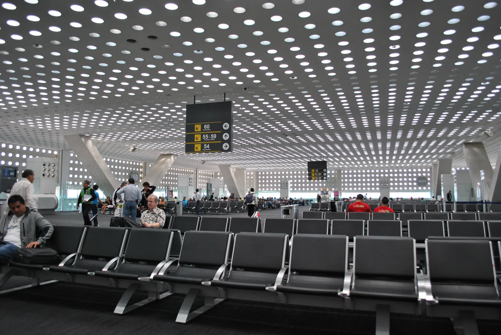 A departure gate lounge in Terminal 2 at Mexico City airport, with rows of black seats under a white ceiling perforated with hundreds of round skylights