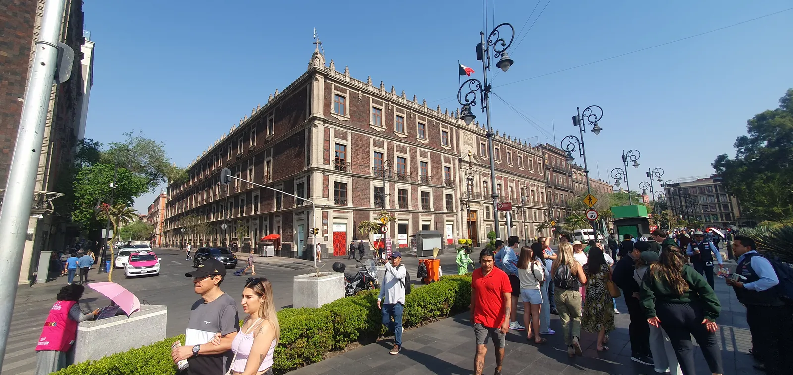 The Nacional Monte de Piedad building on the north-west corner of Mexico City's Zócalo, a long grey stone facade of regular windows above an arcade, with pedestrians and traffic passing in front