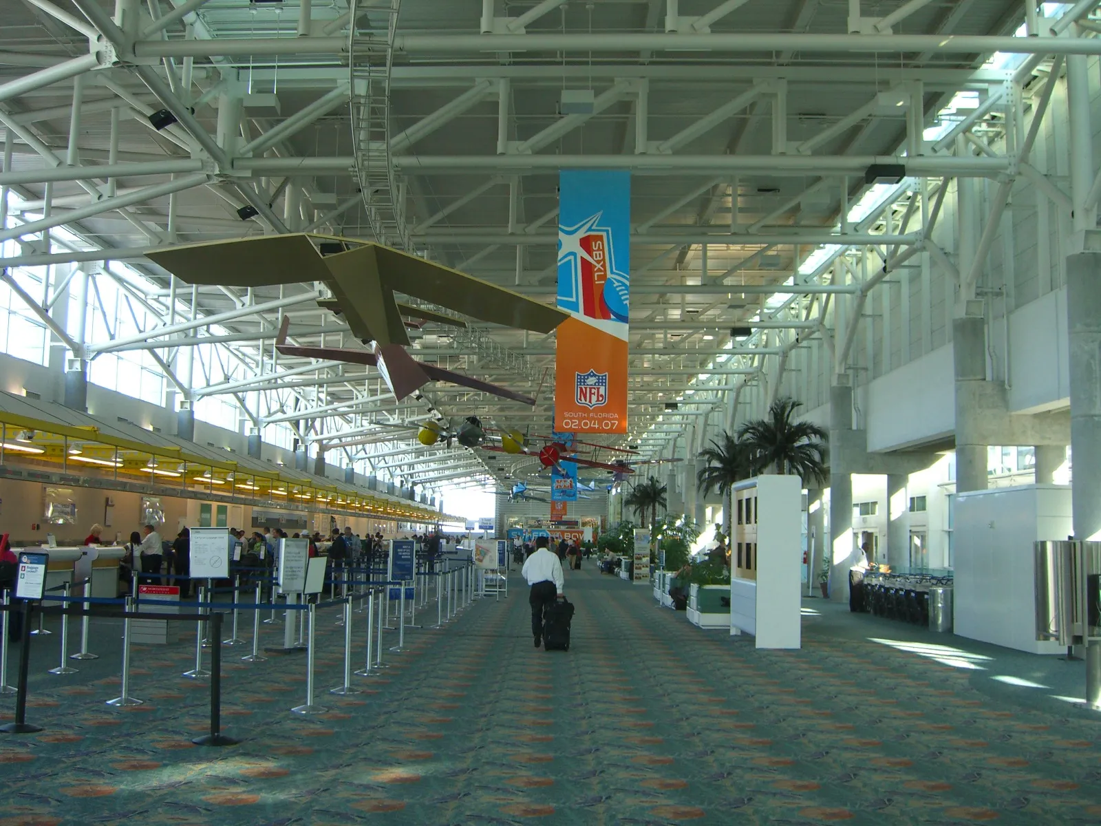 The long check-in hall of Terminal 1 at Fort Lauderdale-Hollywood International Airport, under a white steel roof, with a model plane hanging overhead