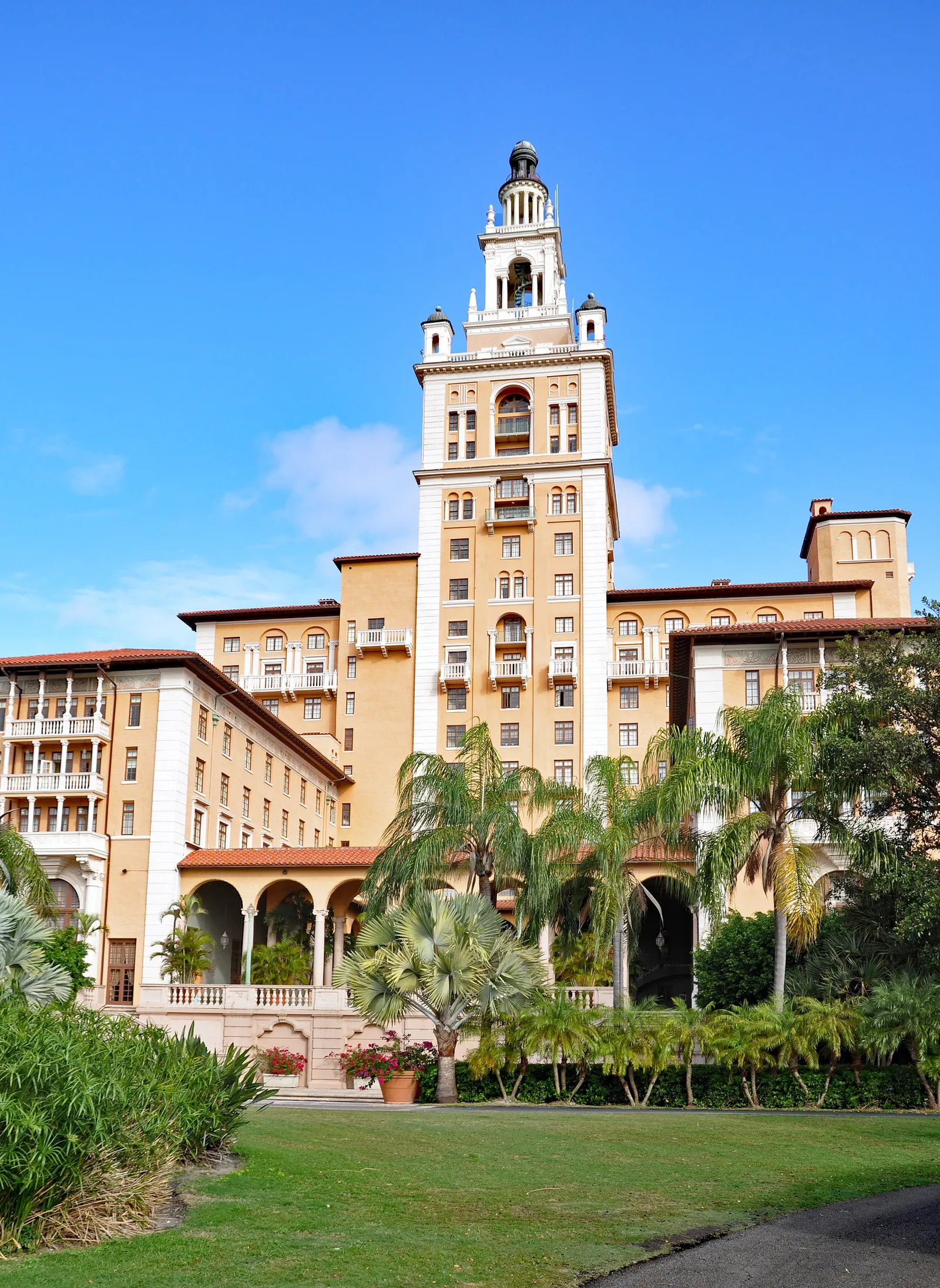 The Biltmore Hotel in Coral Gables, Miami, its tall tiered tower in salmon-colored stucco rising above the hotel's wings, with palms and a lawn in front