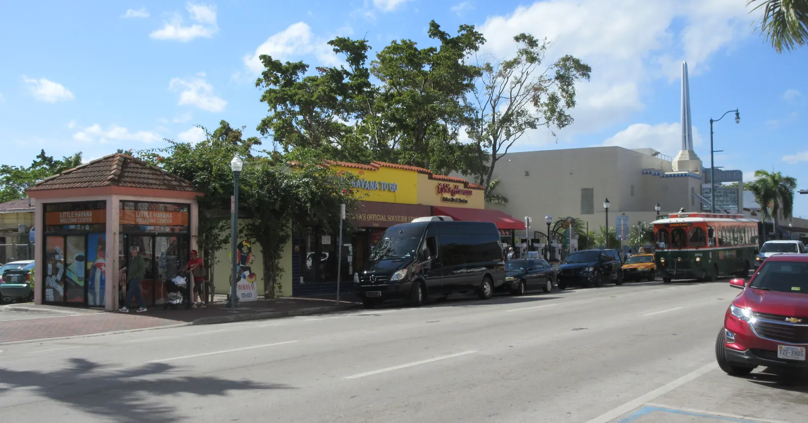 Calle Ocho in Little Havana, Miami, a wide sunny street lined with low shops, the tiled roof of the Domino Park pavilion on the corner and the Tower Theater's white spire rising in the distance