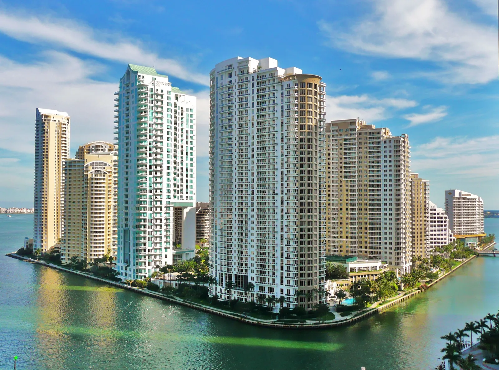 Brickell Key in Miami seen from the north across the water, residential towers in white and cream lining the edge of the man-made island, with a seawall and palms along the shore