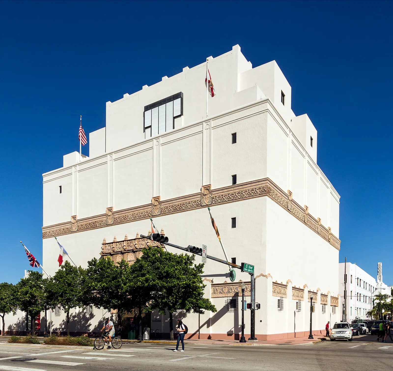 The Wolfsonian museum on Washington Avenue in Miami Beach, a tall white Mediterranean Revival warehouse with few windows, an ornate carved entrance and flags above the street corner