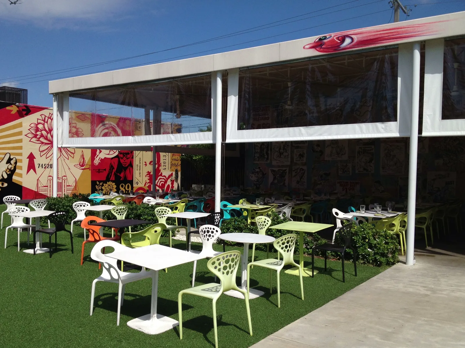The courtyard inside Wynwood Walls in Miami, white tables and chairs on artificial grass under a shade canopy, with murals covering the warehouse walls behind