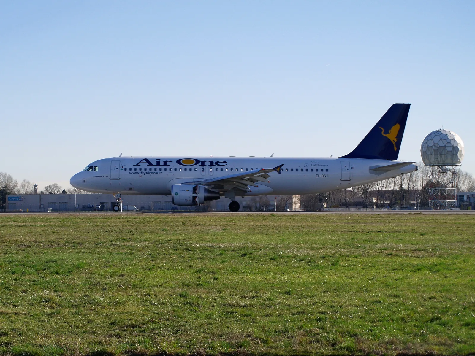 An airplane on the tarmac at Milan Linate Airport with the airport's distinctive radar dome in the background