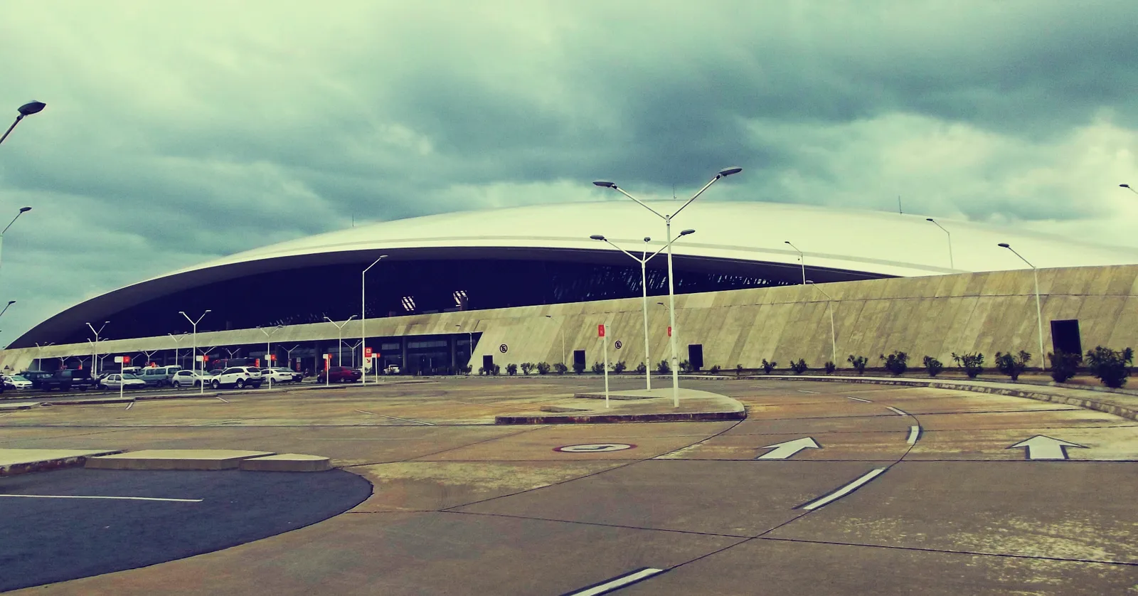 The terminal at Montevideo's Carrasco International Airport seen from the forecourt, a low building under one long curved roof that sweeps in a shallow arc from end to end above the glazed frontage