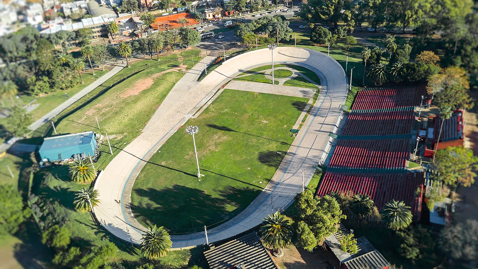An aerial view of the Velódromo Municipal in Montevideo's Parque Batlle, an oval banked cycling track around a grass infield, ringed by palm trees and low red-roofed stands