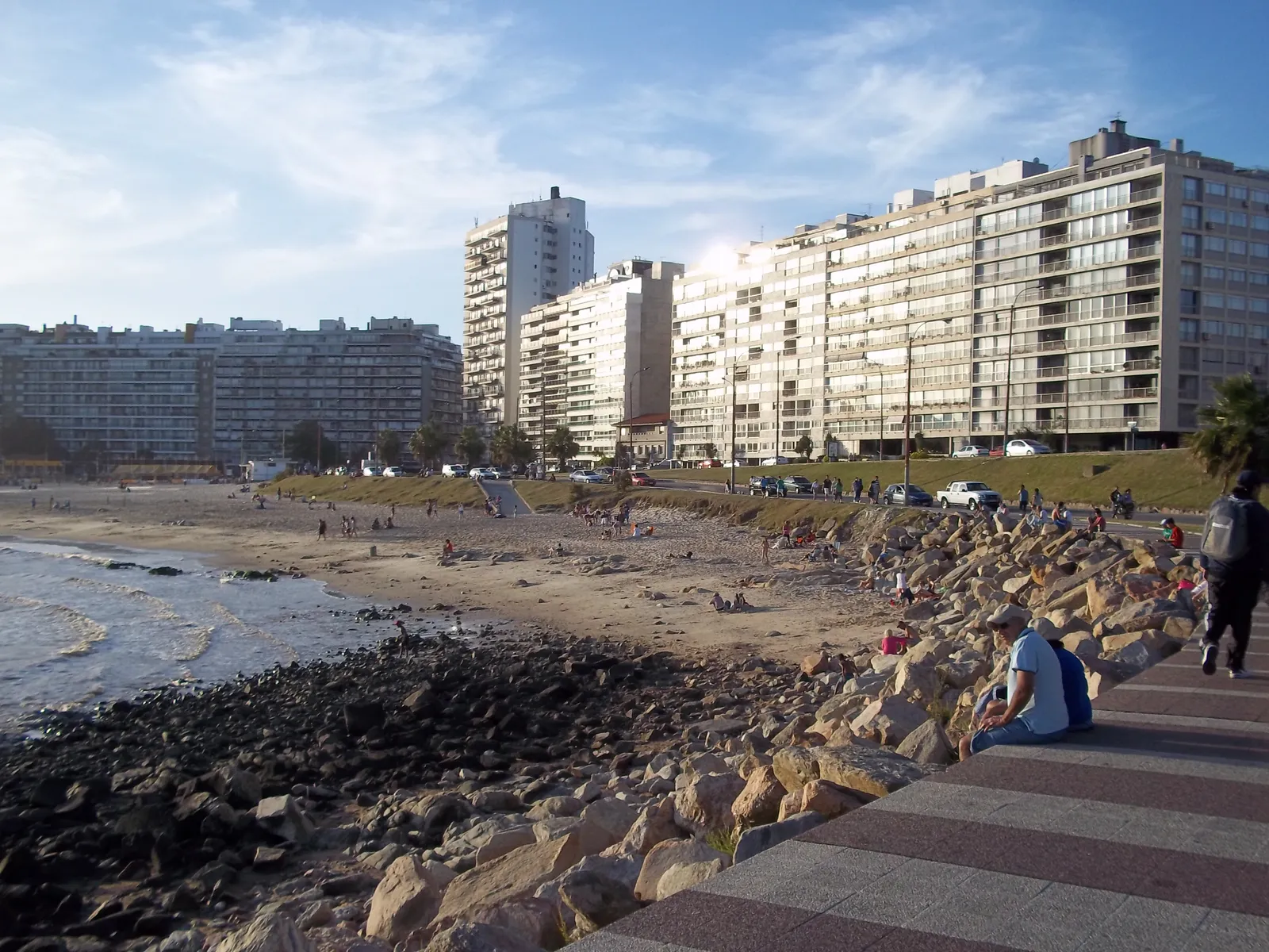 Playa Pocitos in Montevideo seen from the rocky rambla wall, a curve of sand backed by a dense line of white apartment towers along the seafront