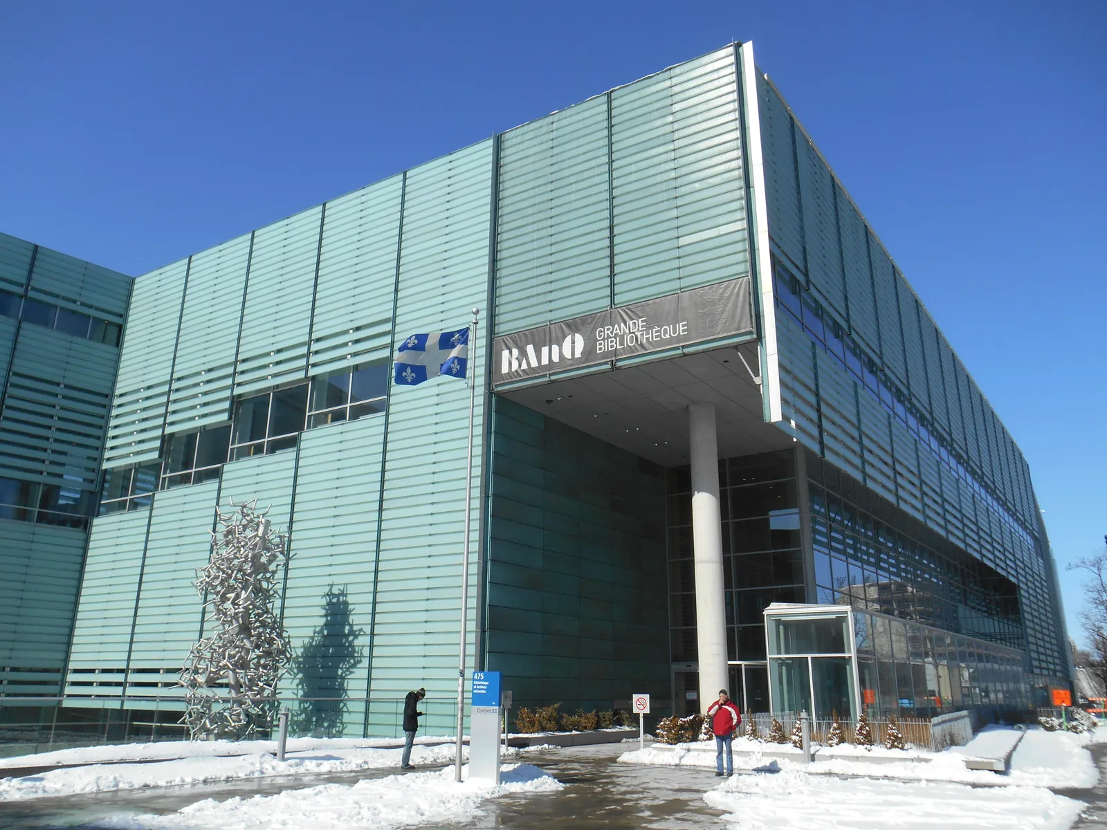 The Grande Bibliothèque in Montreal seen from the street, its walls faced in vertical green-tinted glass slats with the library's name on a dark panel above the glazed entrance