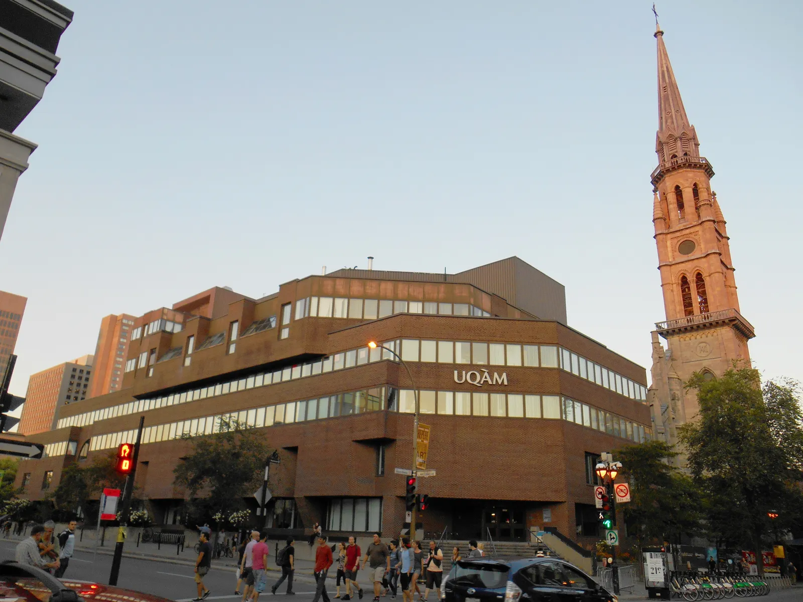 The low brick and glass UQAM pavilion in Montreal with its name along the facade, and the tall pink stone neo-Gothic steeple of the old Saint-Jacques church rising directly beside it