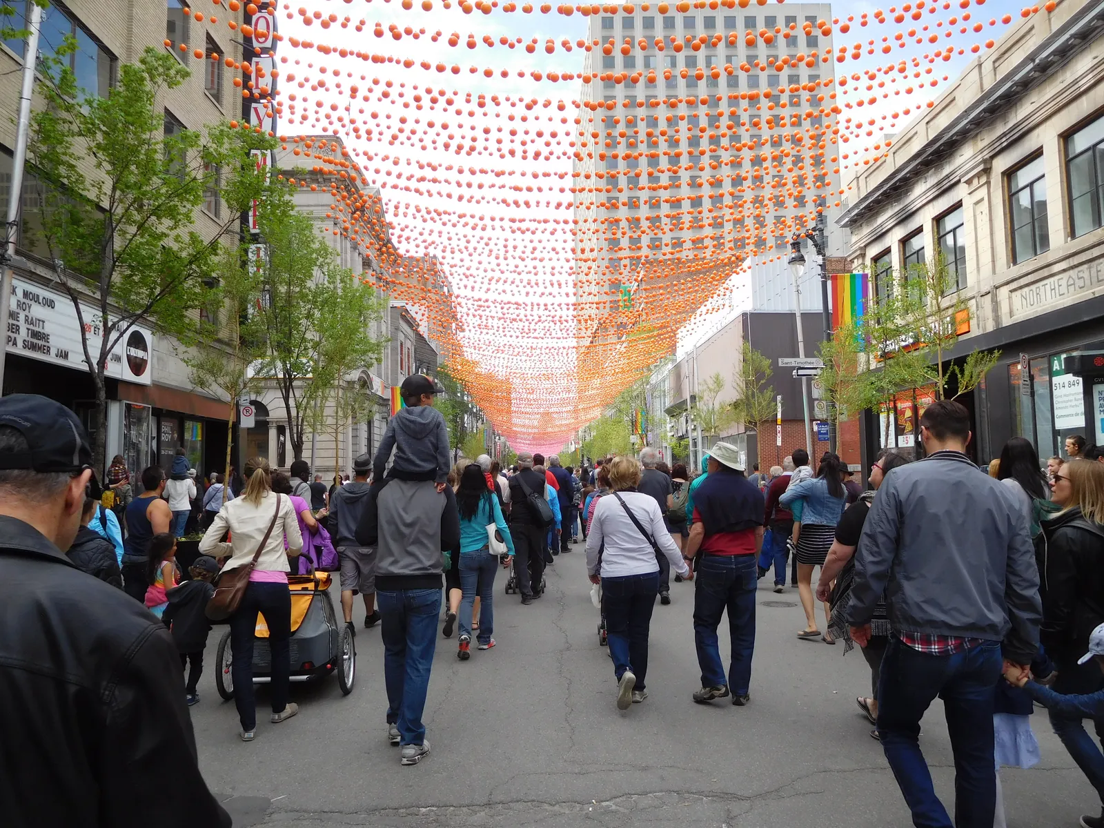 Rue Sainte-Catherine Est in Montreal closed to traffic and filled with people walking down the middle of the road, strings of small coloured spheres suspended overhead between the buildings