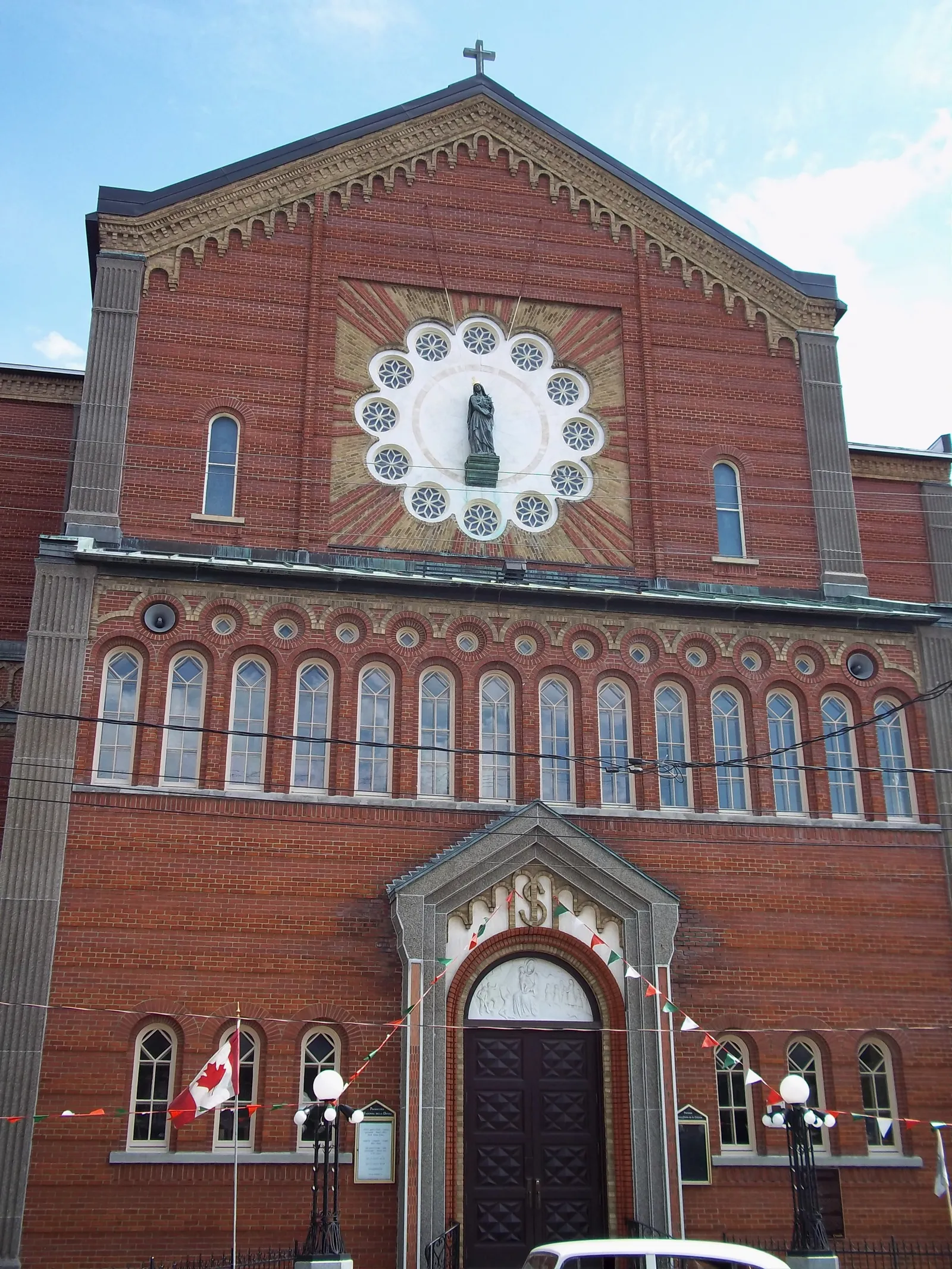 The red brick front of the Madonna della Difesa church in Montreal's Little Italy, a gilded mosaic of the Virgin set into the gable above a row of arched windows, with Italian and Canadian bunting strung across the entrance