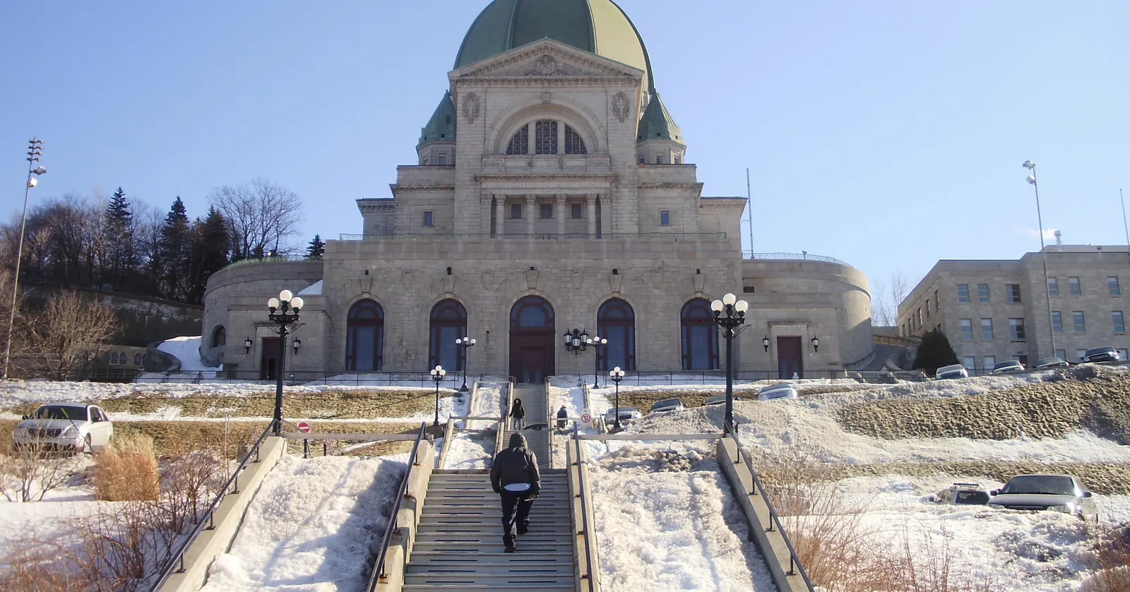 Saint Joseph's Oratory in Montreal seen from the foot of the hill, its green copper dome rising over a pale stone front with the long concrete staircase climbing towards the doors