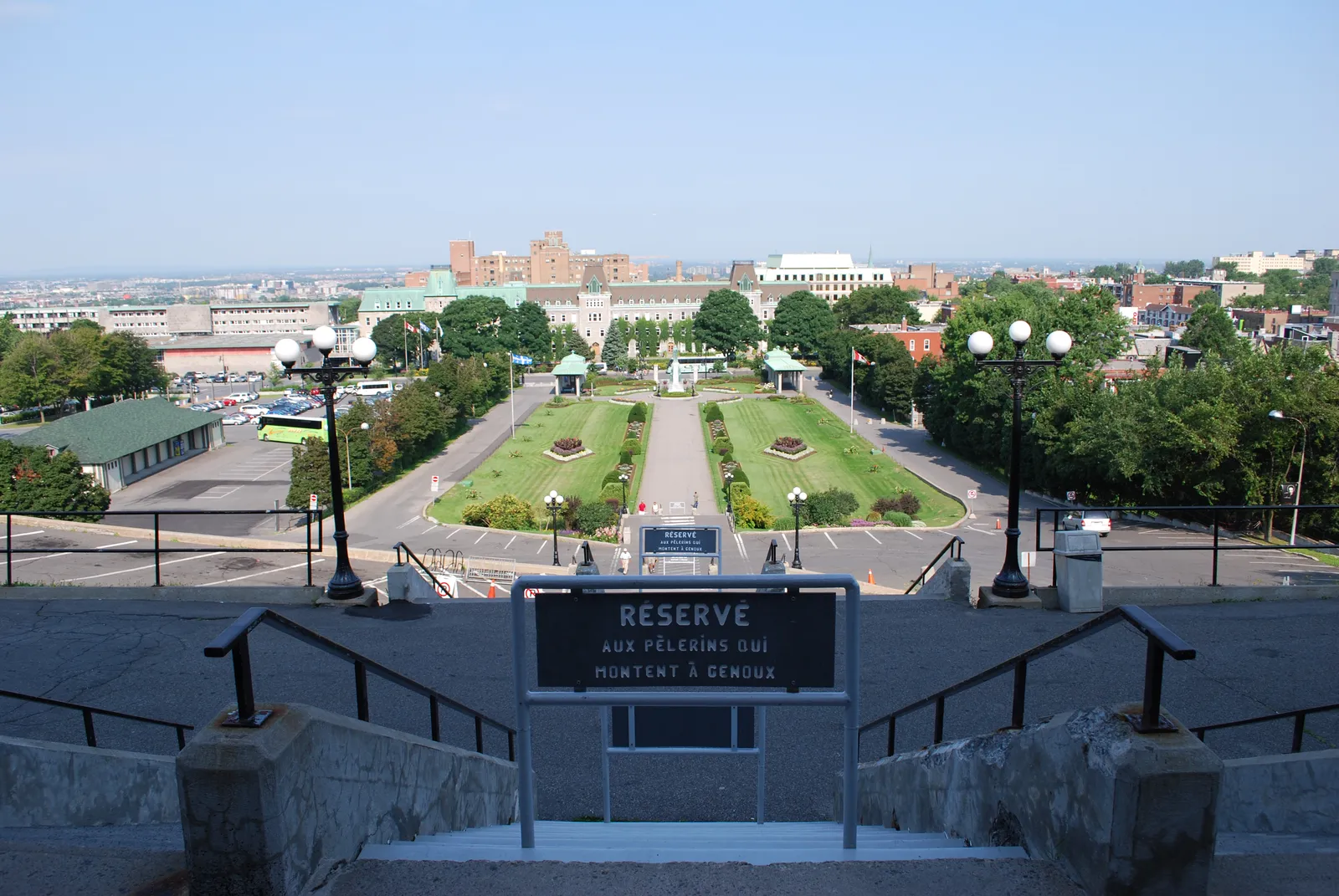 The view down the staircase at Saint Joseph's Oratory in Montreal, a central flight roped off behind a sign reserving it for pilgrims climbing on their knees, with formal gardens and the city beyond