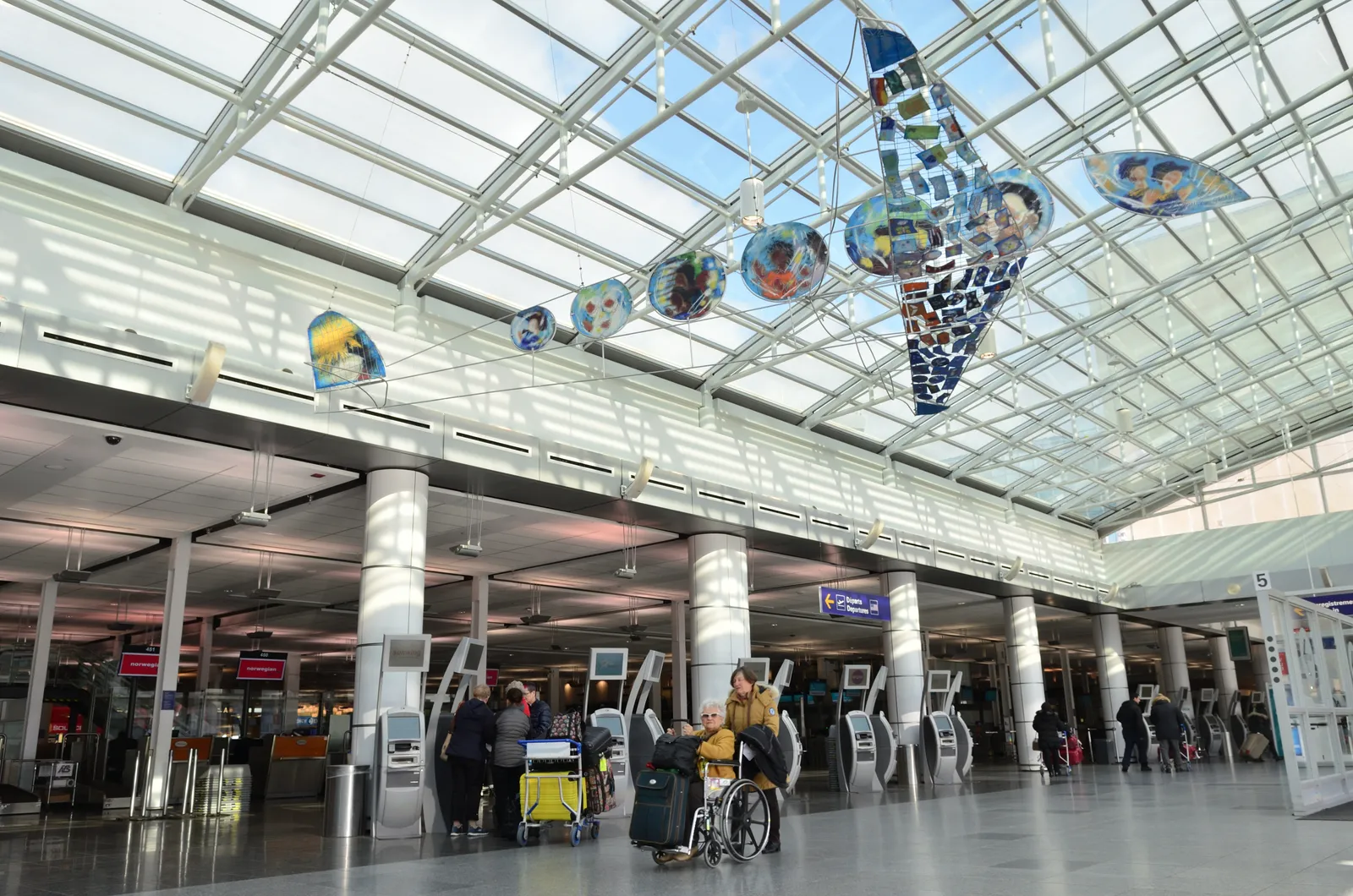 The check-in hall at Montreal-Trudeau airport under a long glass barrel-vaulted roof, with rows of self-service kiosks between white columns and travellers crossing the floor