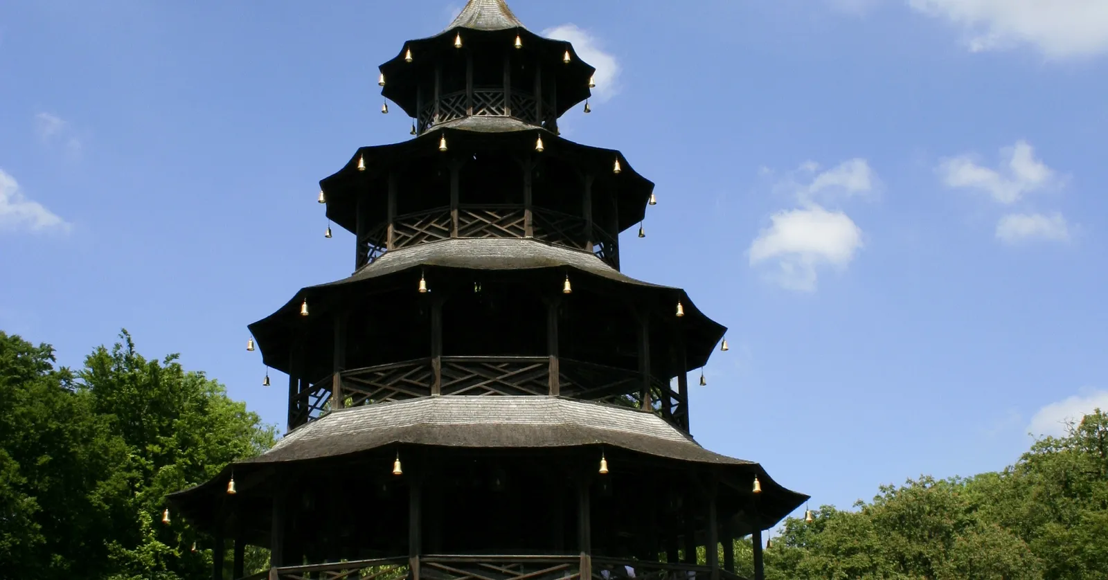 The five-tiered wooden Chinesischer Turm pagoda in Munich's Englischer Garten rising above the treeline against a clear blue sky, small brass bells hanging from each tier