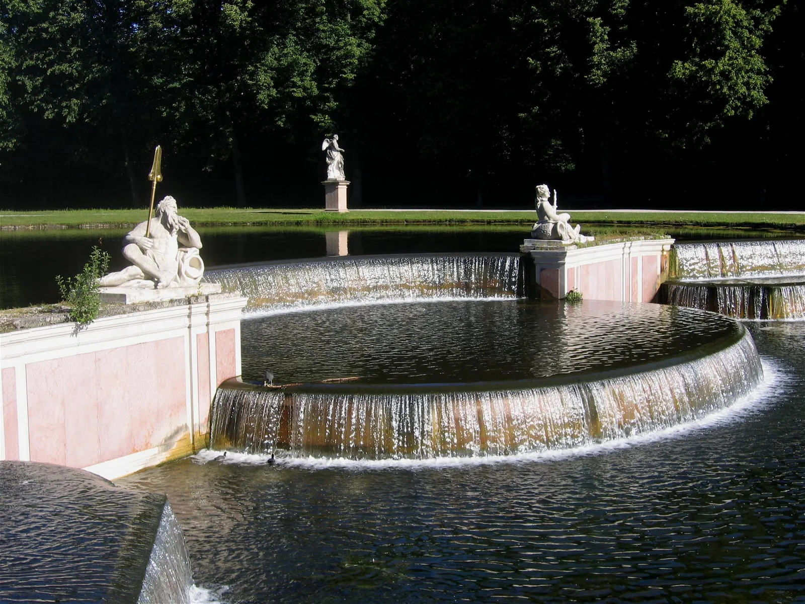 The Große Kaskade fountain in Nymphenburg's palace park, water spilling over pink marble steps past stone statues into a curved basin