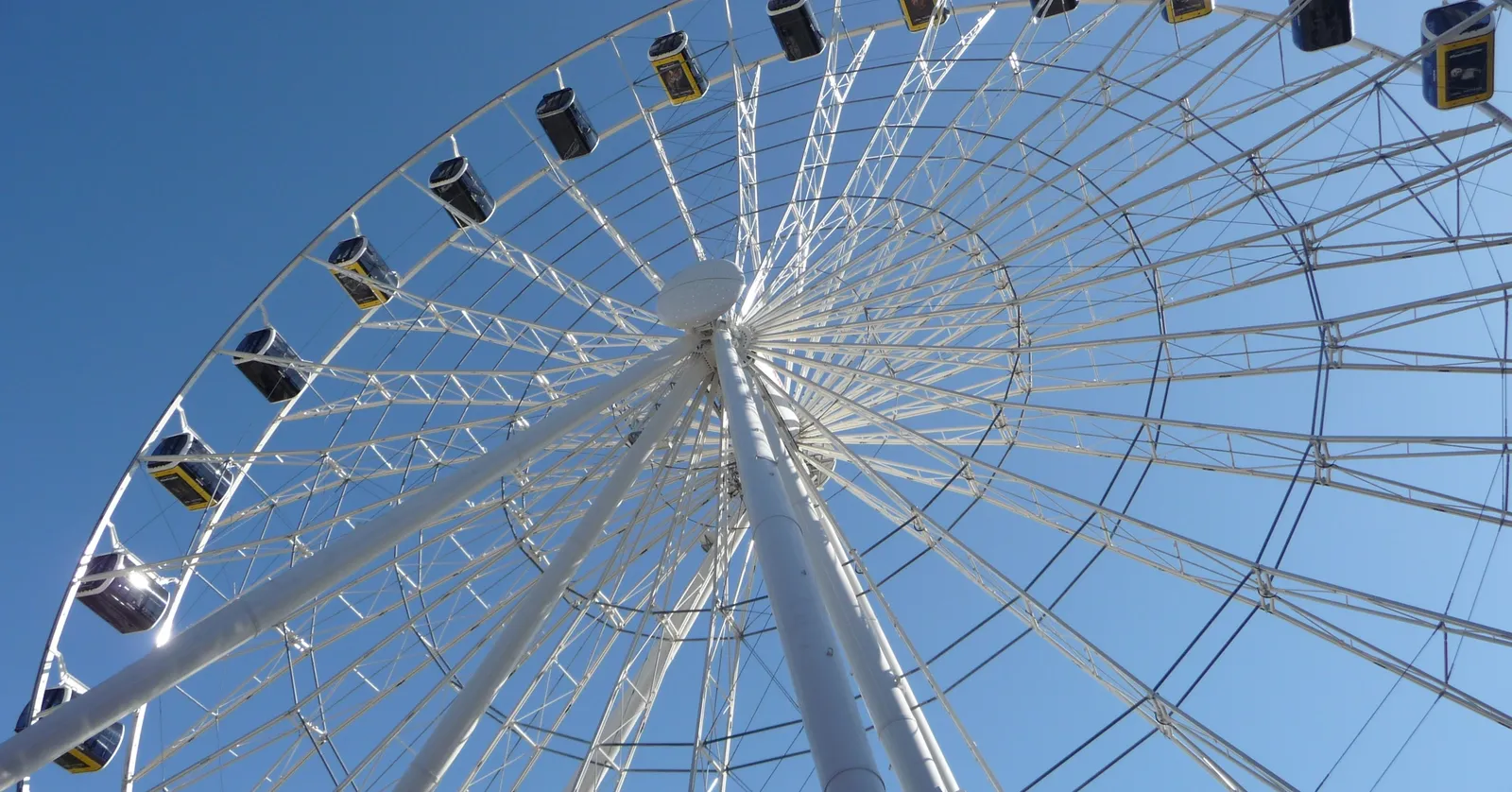 Looking straight up through the white steel structure of the Umadum Ferris wheel in Munich's Werksviertel against a clear blue sky, gondolas hanging around the rim