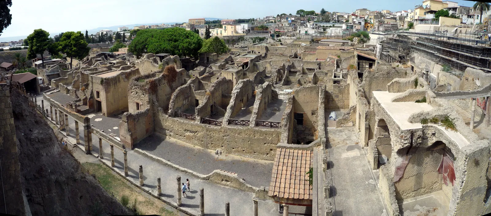The excavated Roman town of Herculaneum seen from the walkway above, its roofless brick houses sunk in a deep pit with the modern town of Ercolano built along the rim