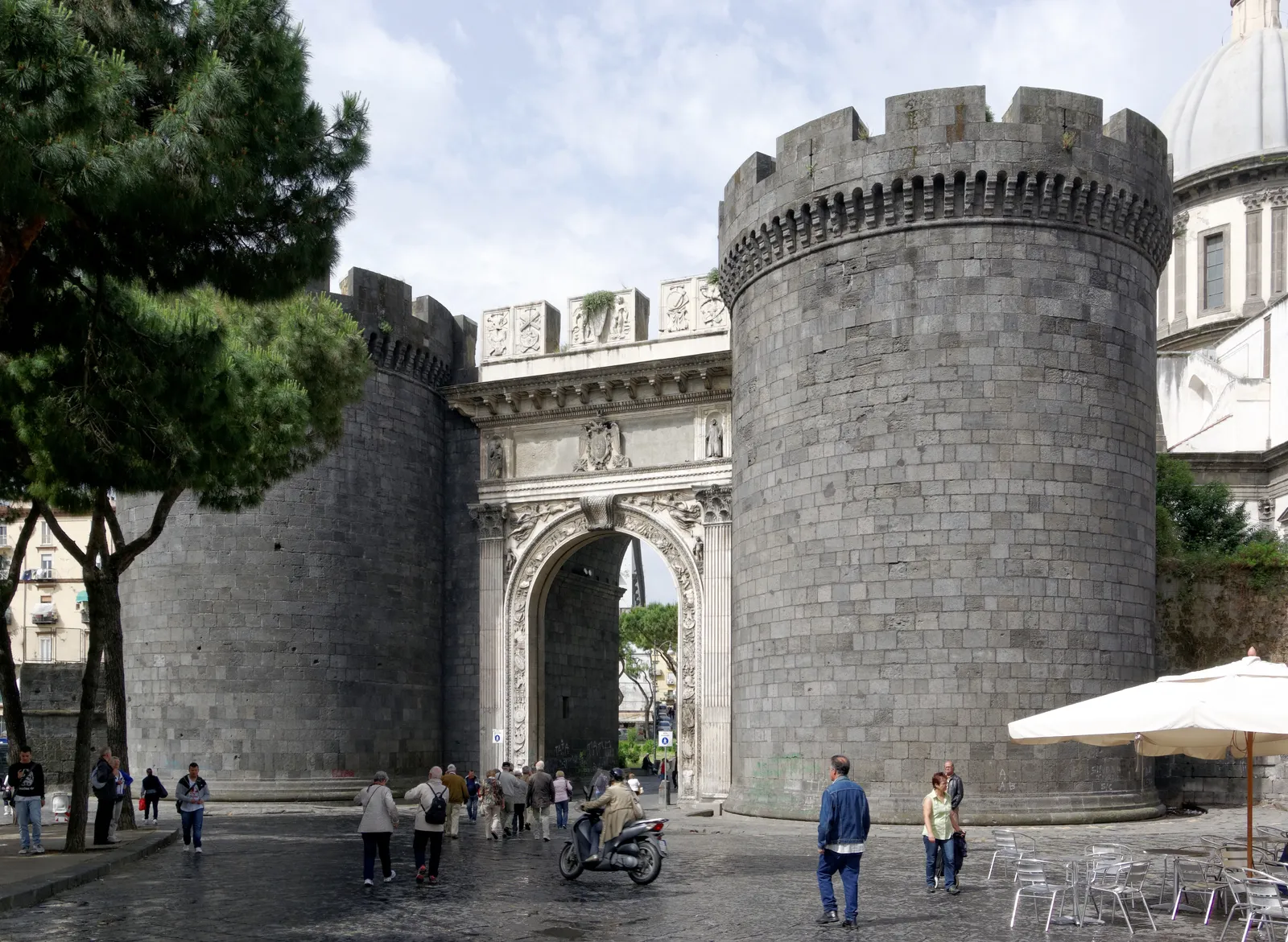 Porta Capuana in Naples, a carved white marble arch set between two dark grey stone towers, with people crossing the square in front of it