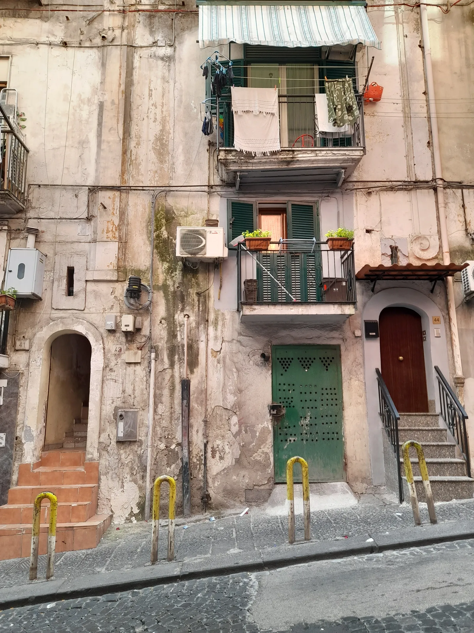 A house front in the Quartieri Spagnoli in Naples, laundry hung over a balcony, green shuttered windows and a studded green door above a steep stepped street